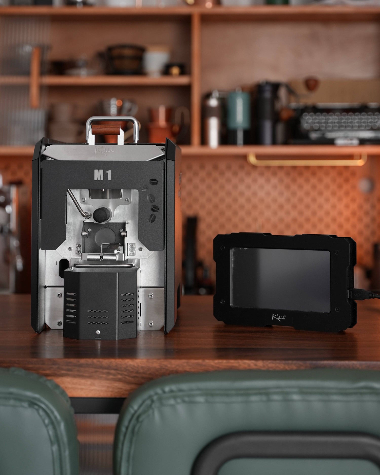 KALEIDO M1 coffee roaster machine with touchscreen control panel on wooden countertop in cozy kitchen setting, showcasing compact design and advanced features for home roasting