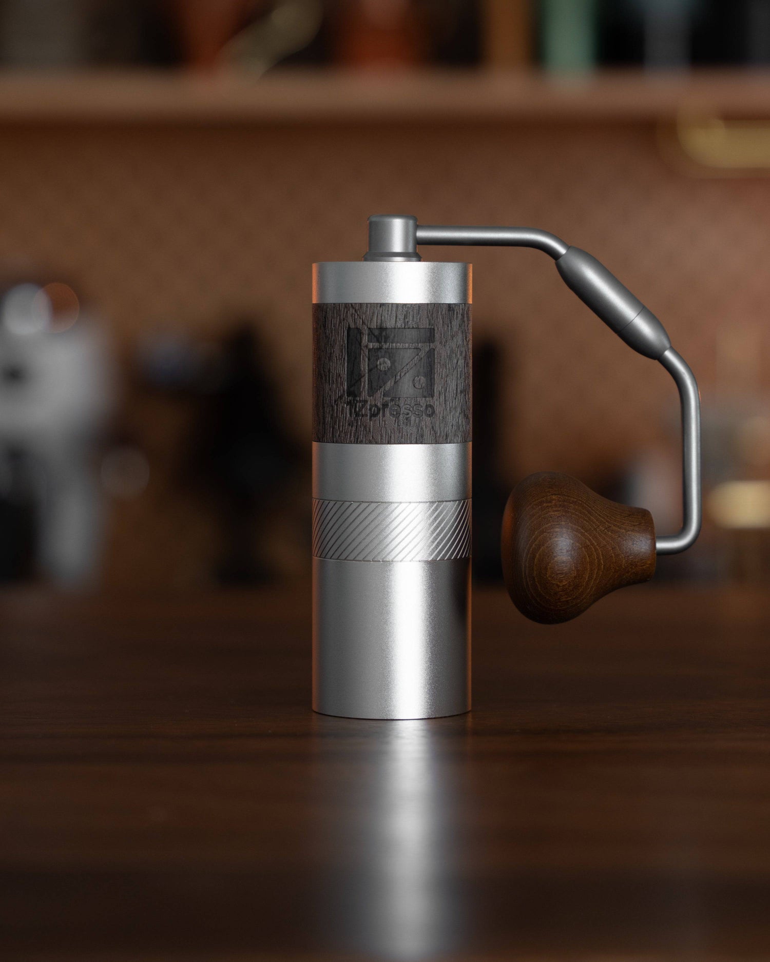 1Zpresso QS2 manual coffee grinder with foldable handle, compact silver and wood design, standing on wooden surface in kitchen setting