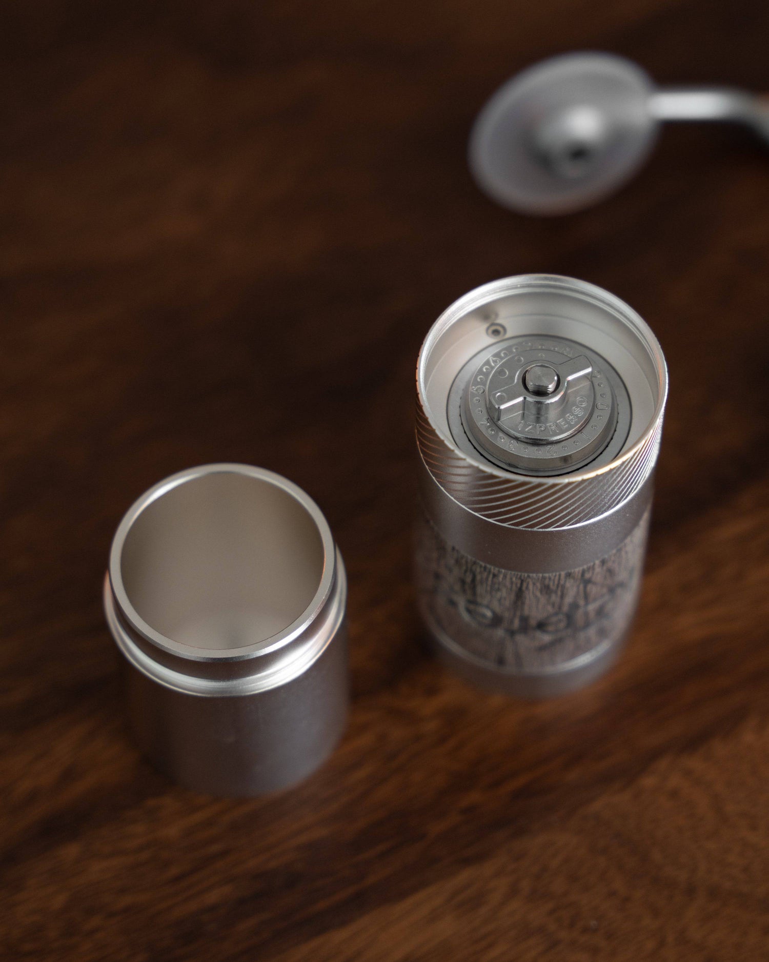 1Zpresso QS2 manual coffee grinder disassembled on wooden surface, showcasing compact design, stainless steel body, and precision grinding mechanism for portable, high-quality coffee grinding