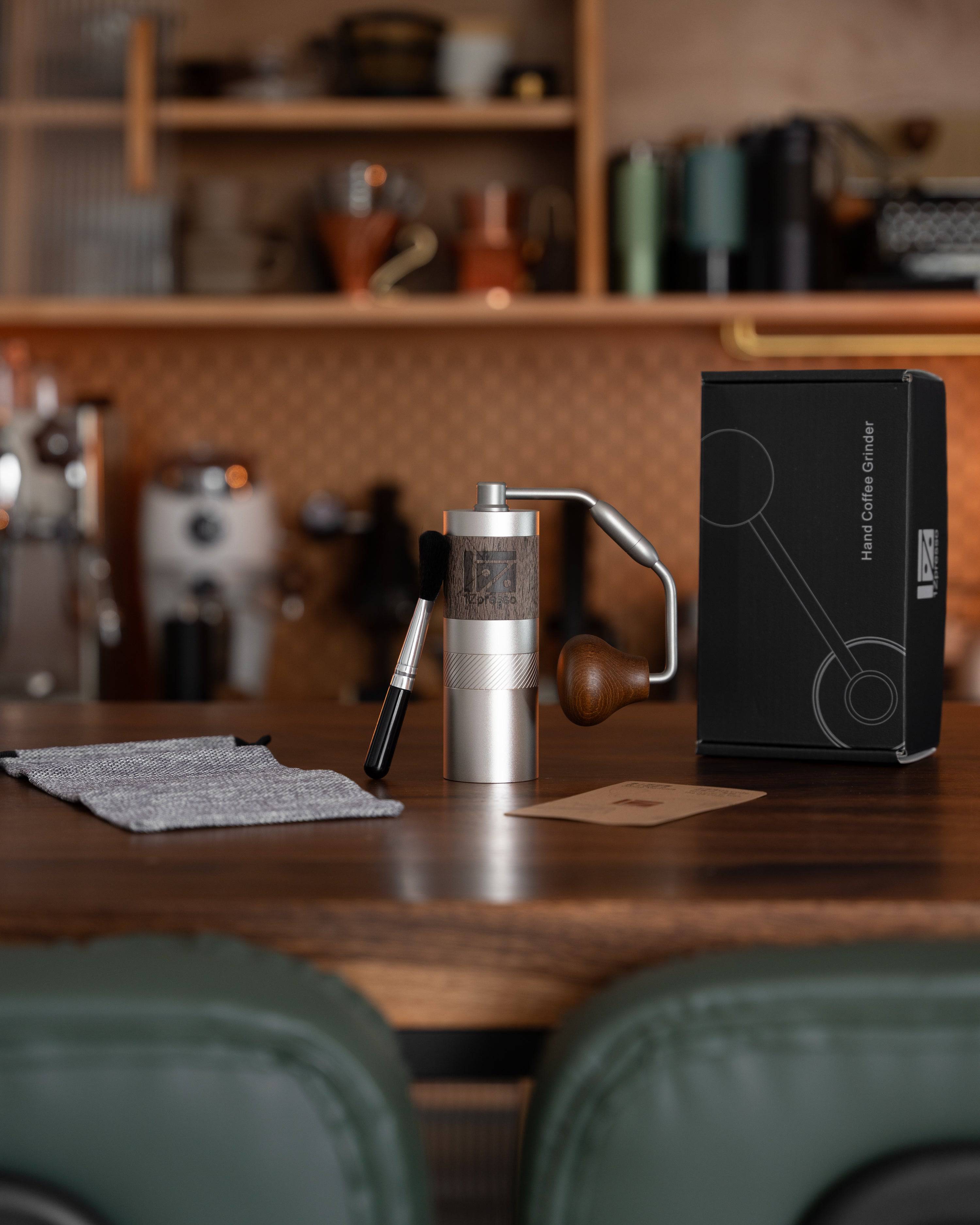 1Zpresso QS2 manual coffee grinder on wooden table with packaging, in a stylish kitchen setting, showcasing compact design and premium quality for coffee enthusiasts