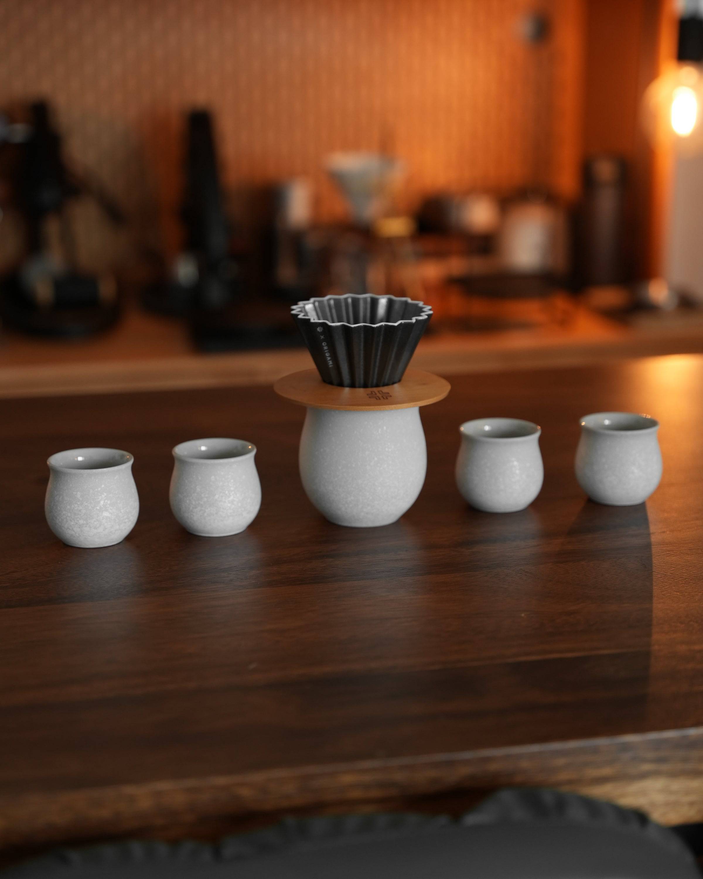 Ninety Plus Coffee Kone Ring 10.1 walnut stand with mini brewing filter cup, displayed alongside white ceramic cups on wooden surface in cozy coffee setting