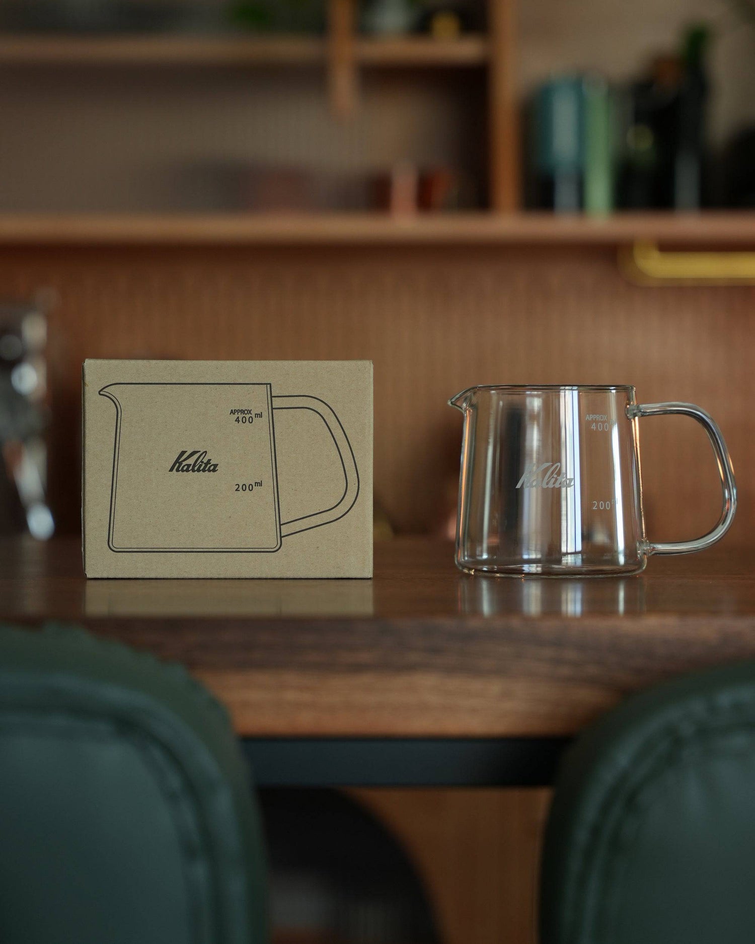 Kalita JUG400 heat-resistant glass coffee jug displayed on wooden table with product box, showcasing its elegant design, clear measurement markings, and comfortable handle for perfect pour-over coffee brewing