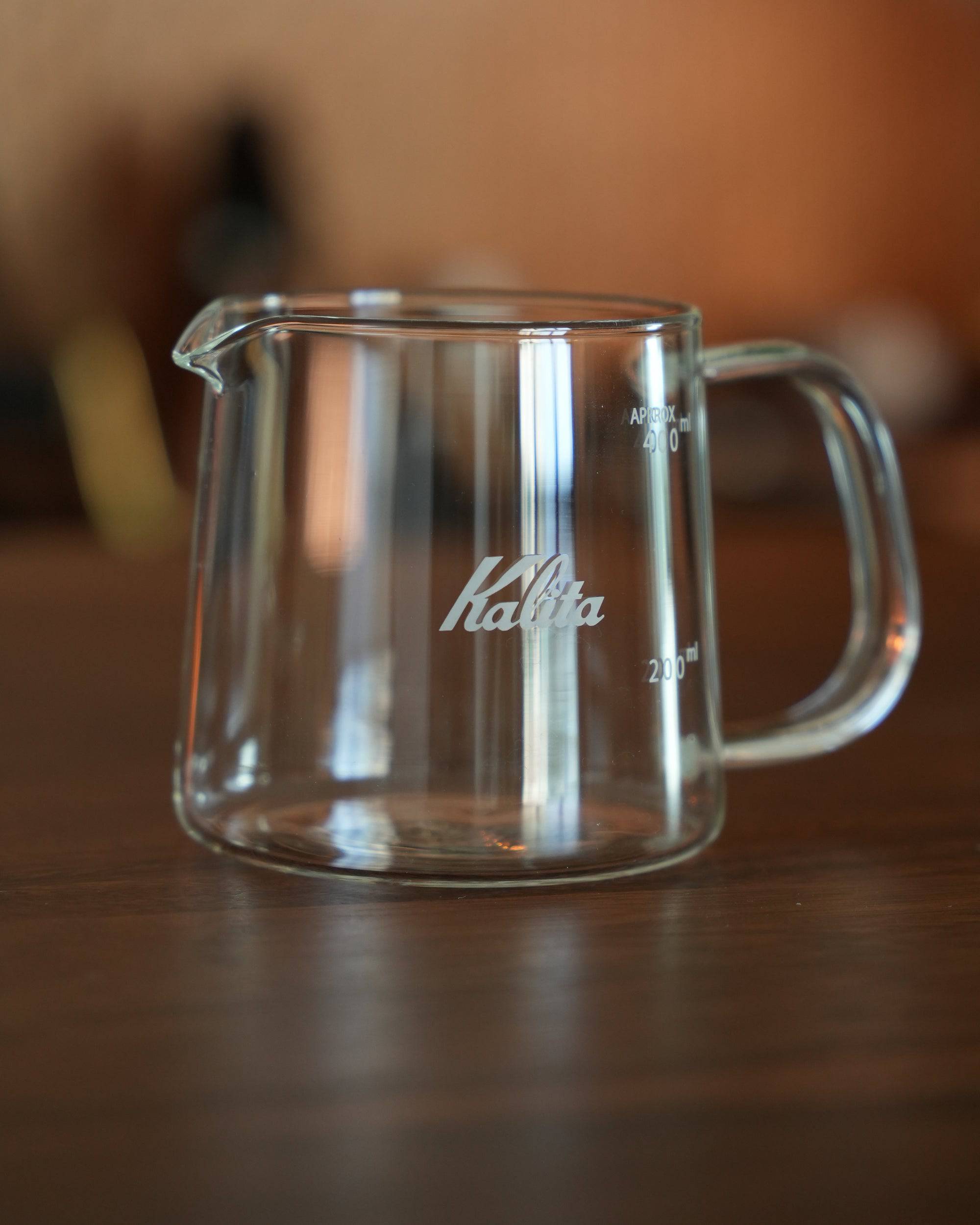 Kalita JUG400 heat-resistant glass coffee pot, 400ml capacity, with clear measurement markings and Kalita logo, featuring a sturdy handle and spout for easy pouring, placed on a wooden surface