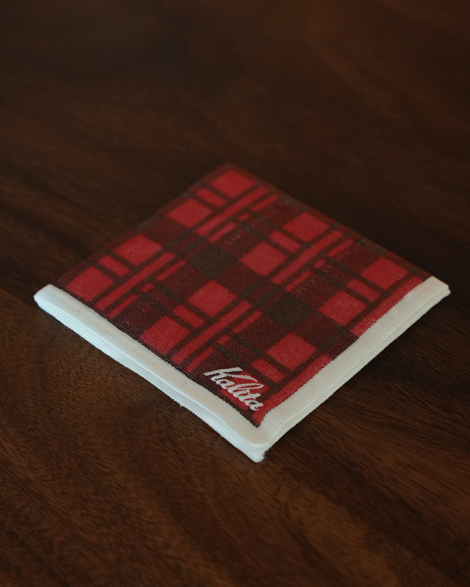 Kalita classic red plaid coffee cloth on wooden surface, folded neatly displaying brand logo, showcasing high-quality cotton material and stylish design for pour-over coffee enthusiasts