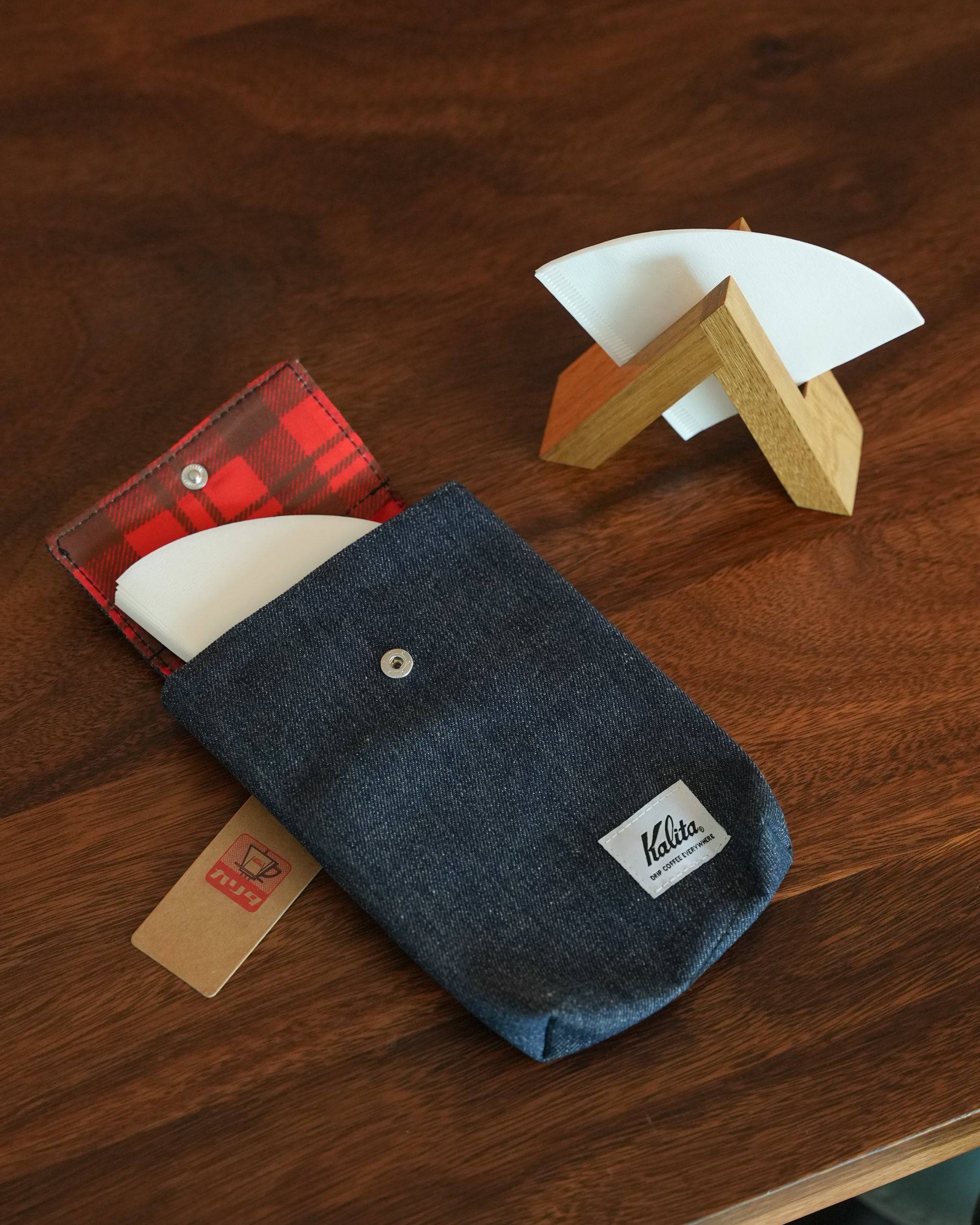 Denim Kalita coffee filter storage pouch with red plaid lining, displayed with wooden filter holder and coffee filters on wooden surface
