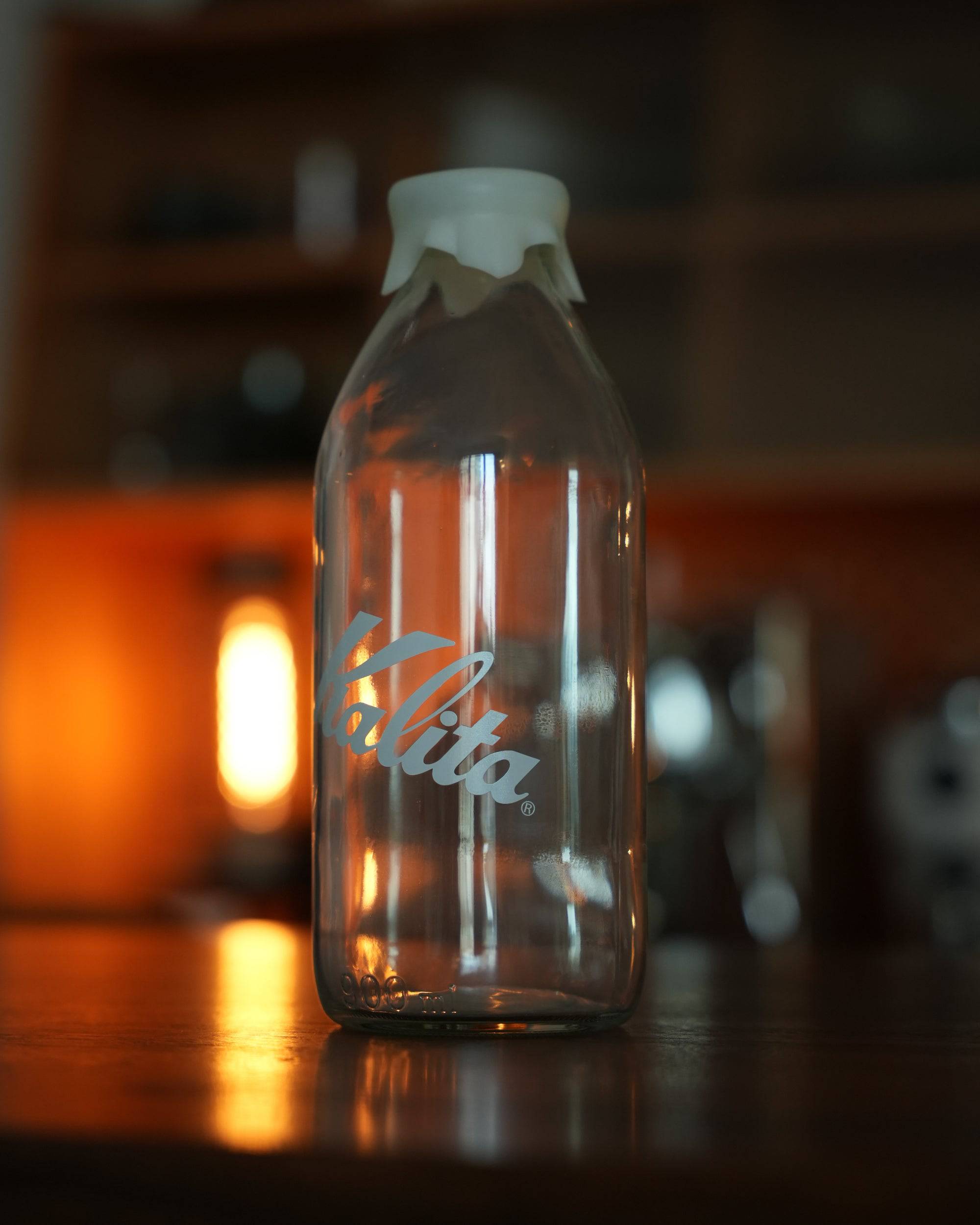 Kalita glass milk bottle shaped coffee bean storage jar, 320g capacity, with white lid, illuminated by warm ambient lighting, showcasing stylish design for coffee enthusiasts