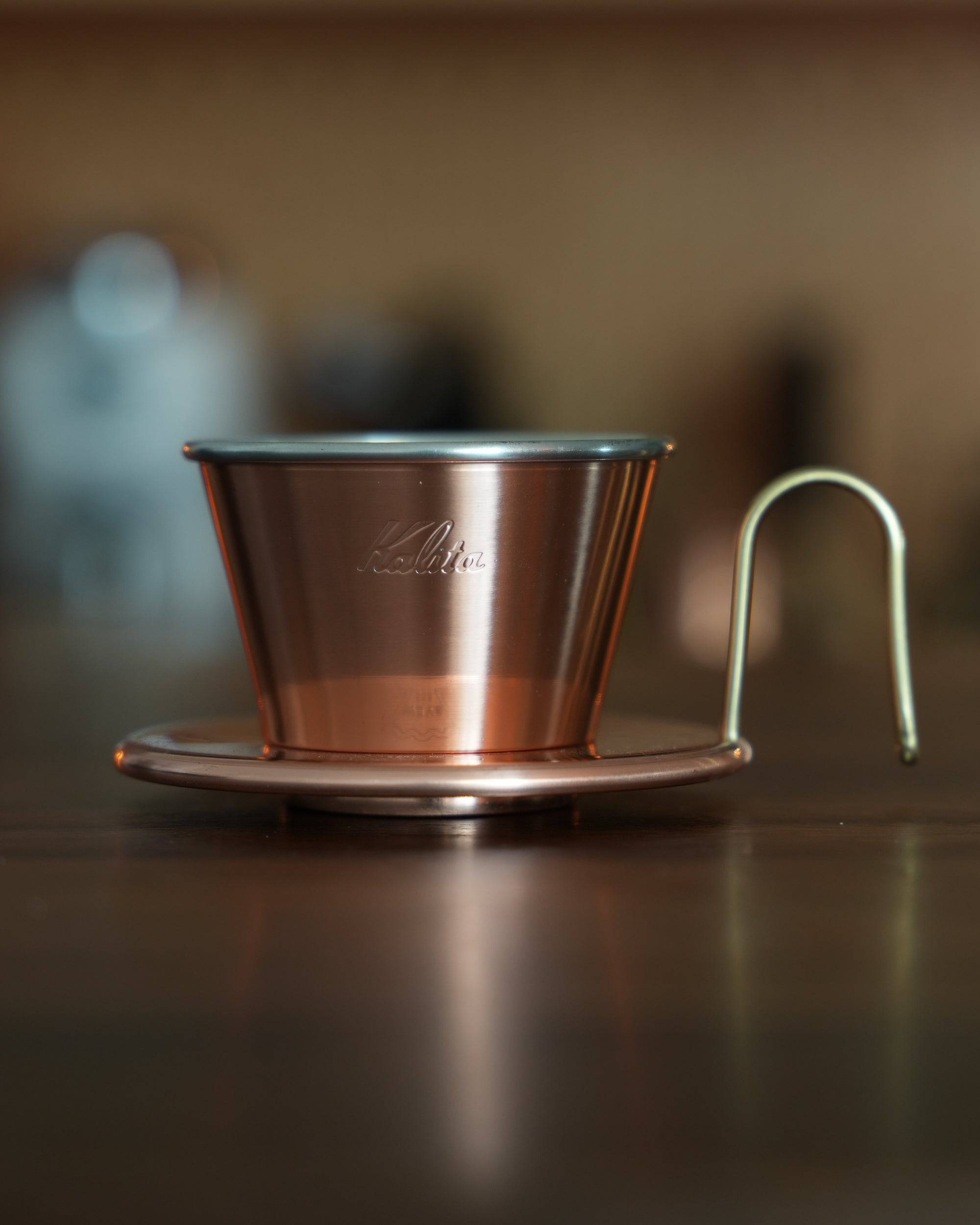 Kalita copper pour-over coffee dripper with three-hole design and metal stand, showcasing elegant craftsmanship and superior heat conductivity for optimal brewing