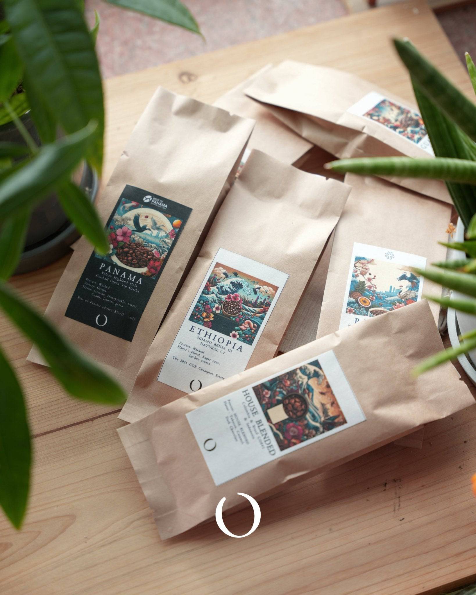 Artistically packaged coffee bags from Ana Sora farm, featuring colorful labels with intricate designs, displayed on a wooden surface surrounded by green plants, showcasing premium Ethiopian coffee products