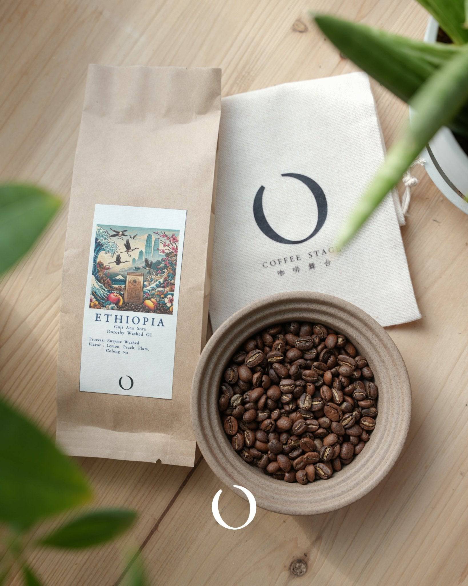 Ethiopia Ana Sora coffee beans in ceramic bowl, packaging with colorful label, and branded cloth bag on wooden surface with plant leaves in foreground, showcasing premium specialty coffee product