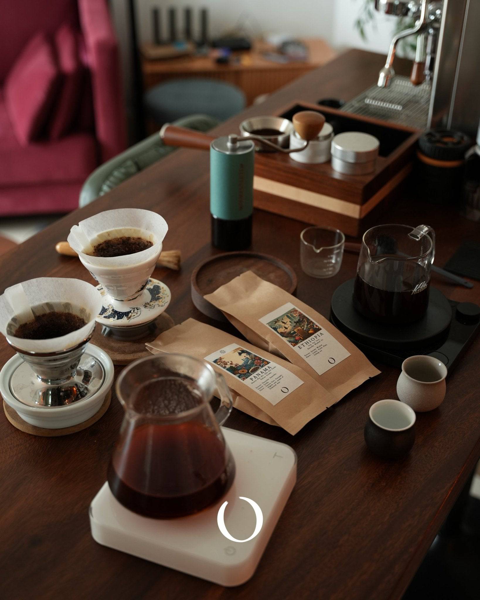 Coffee brewing setup with pour-over filters, coffee bags, scale, grinder, and espresso machine on wooden table, showcasing Ana Sora Ethiopian coffee preparation