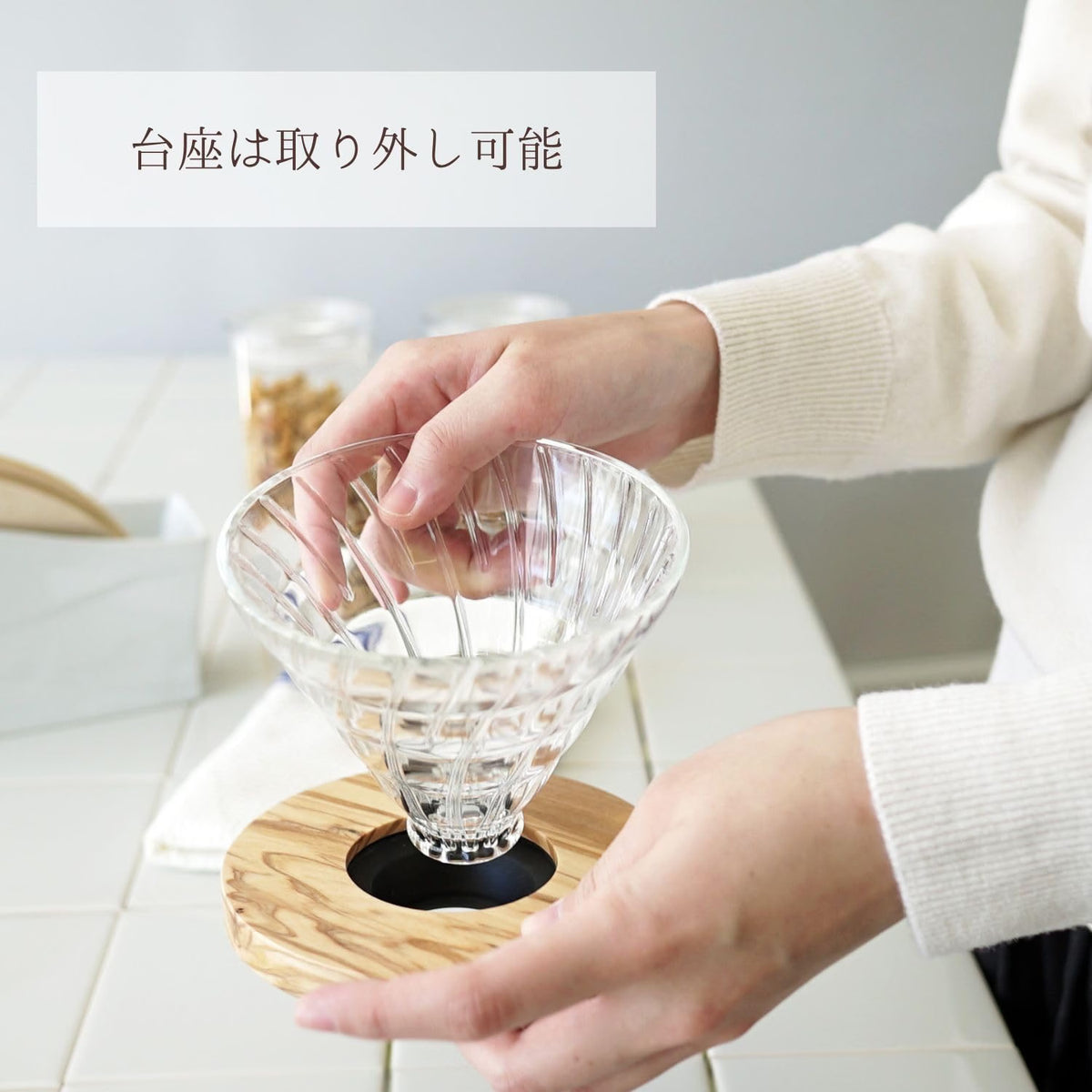 HARIO V60 02 olivewood model, heatproof glass with an olivewood base, 1–4 cups: Hands lift the clear glass dripper from the olivewood base, showing that the two parts separate.