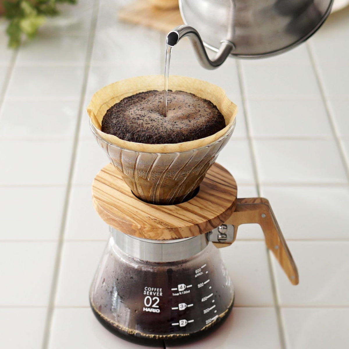 HARIO V60 02 olivewood model, heatproof glass with an olivewood base, 1–4 cups: V60 02 brewing over a glass server; the kettle and glass server are scene props.