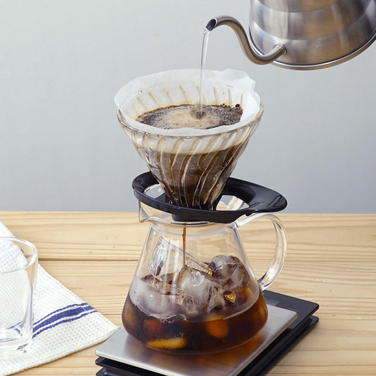 HARIO V60 02 black heatproof glass dripper, 1–4 cups: V60 02 brewing over a graduated glass server; the kettle, glass server and scale are scene props.