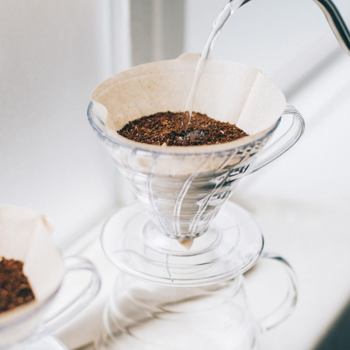 HARIO V60 01 clear resin (1–2 cups) and V60 03 clear resin (1–6 cups), shared image: 01 / 03 dripper models are shown in a brewing scene with coffee dripping from the dripper into a glass server; the kettle and glass server are scene props.