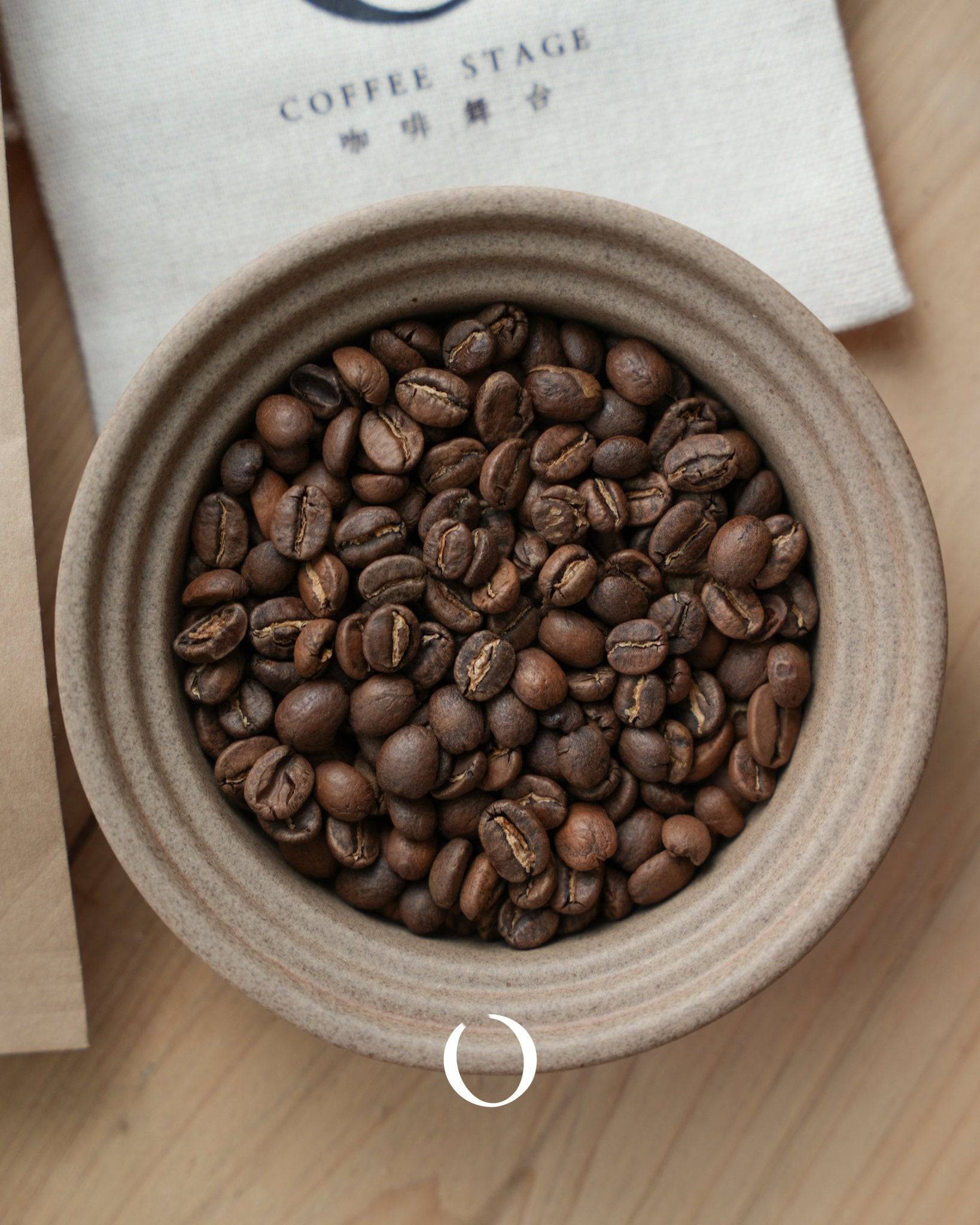 Freshly roasted coffee beans from La Flor del Cafe plantation in Guatemala, displayed in a ceramic bowl next to a branded cloth bag, showcasing the premium quality of Antigua coffee