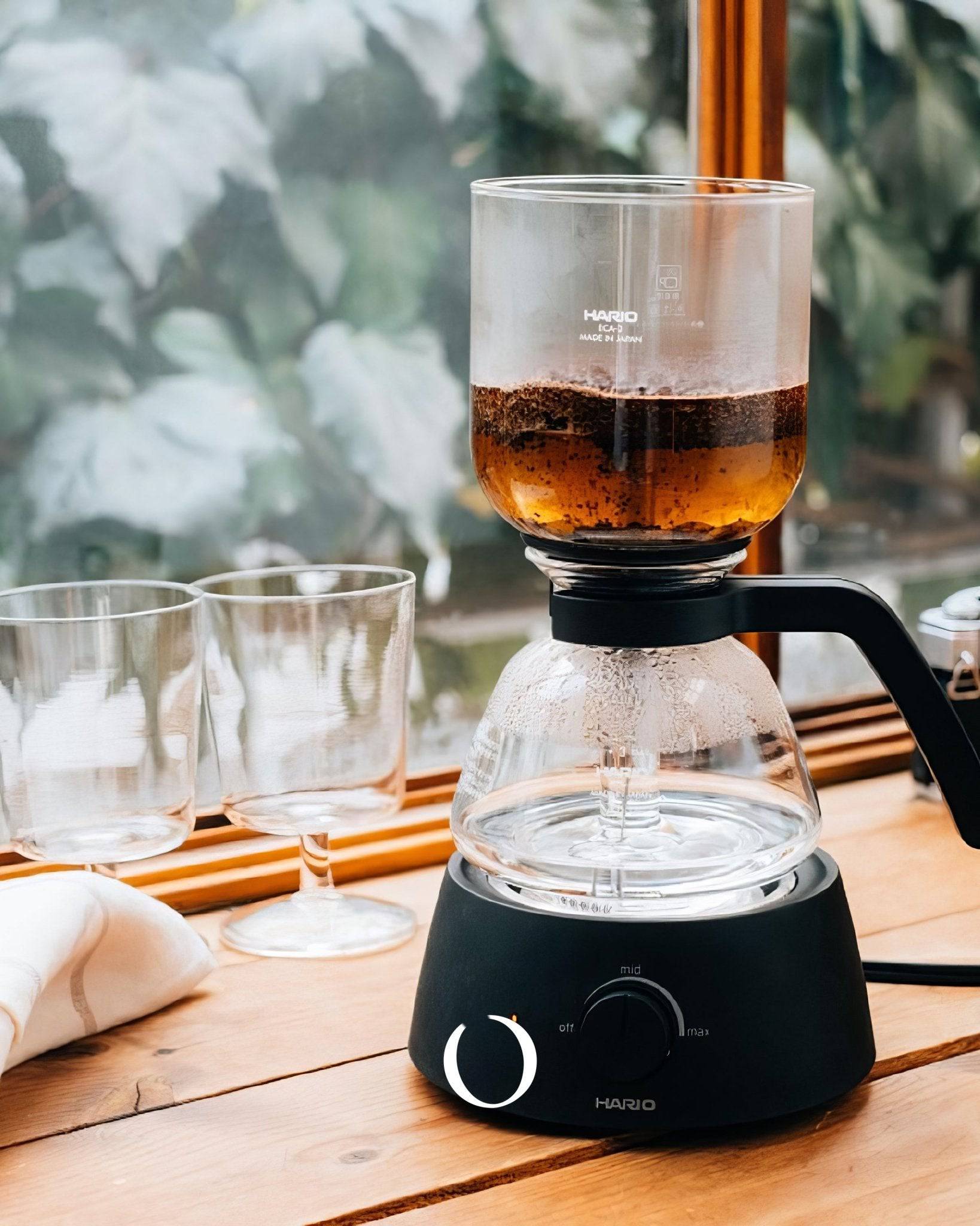 HARIO electric siphon coffee maker brewing coffee on wooden table with glass cups, showcasing unique extraction process and elegant design for premium home brewing experience