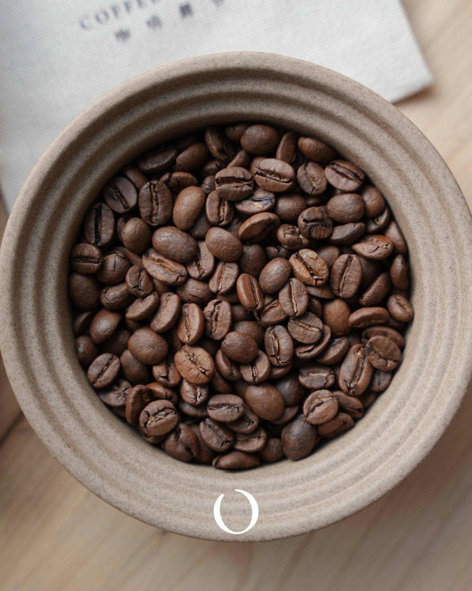 Freshly roasted coffee beans from Colombia, Brazil, and Indonesia blend in a ceramic bowl, showcasing rich brown hues and distinct coffee bean shapes, perfect for House Blended premium coffee mix