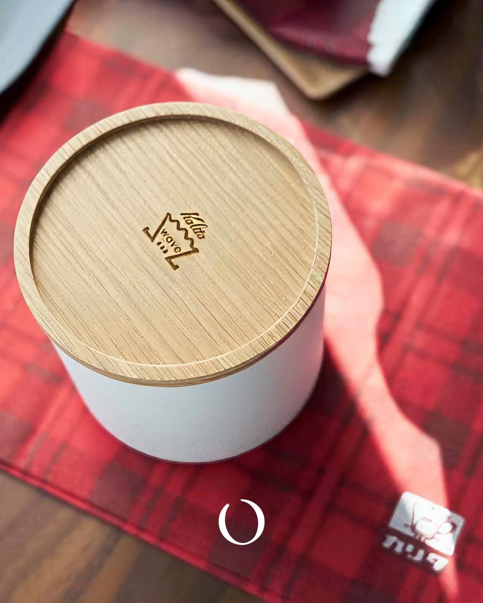Kalita 155/185 Roshi filter paper container with wooden lid on red plaid cloth, showcasing elegant design for coffee enthusiasts. White cylindrical body with Kalita logo engraved on top, perfect for storing and protecting coffee filters.