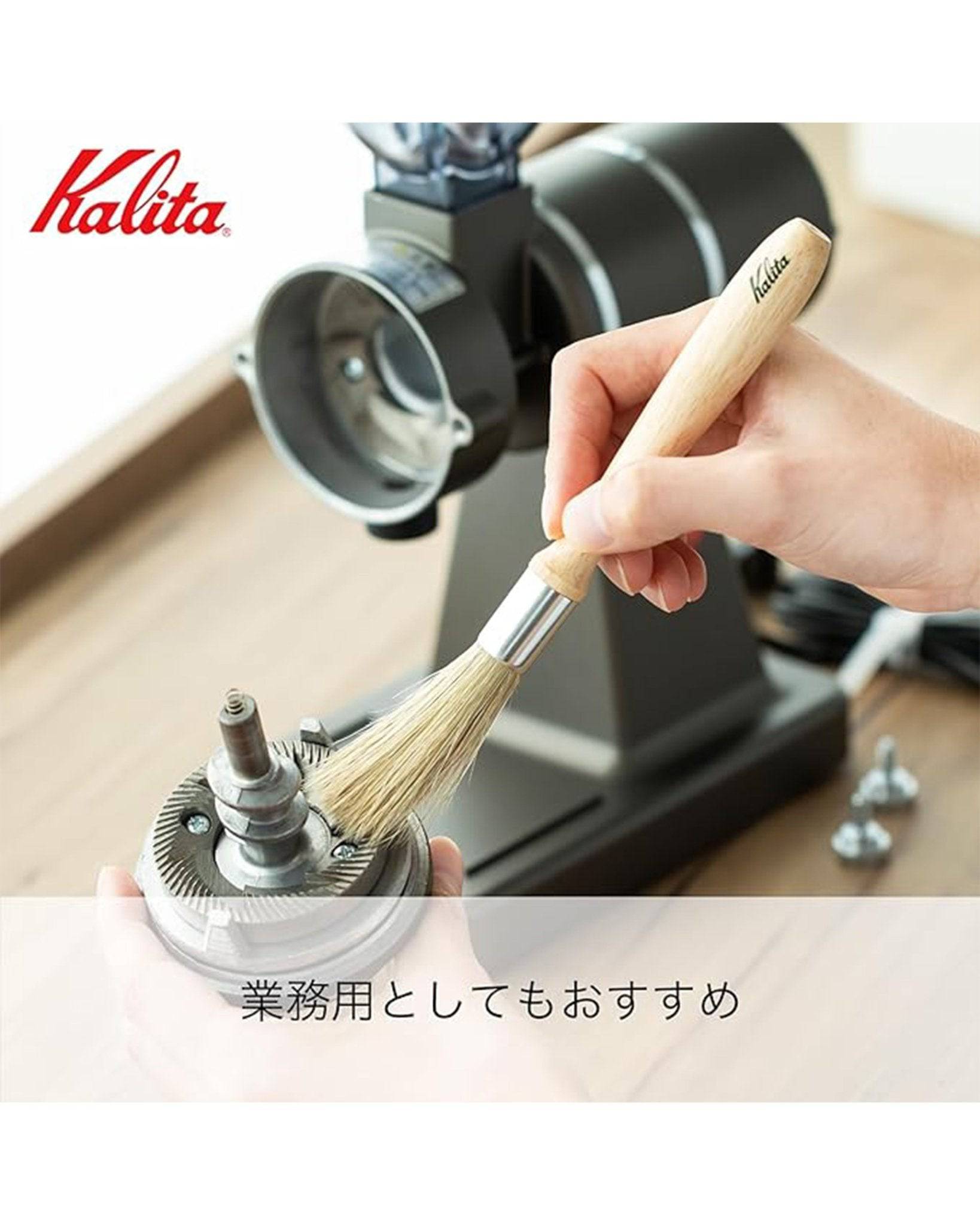 Kalita coffee cleaning brush with wooden handle being used to clean coffee grinder burrs, showcasing its professional-grade quality and effective cleaning action