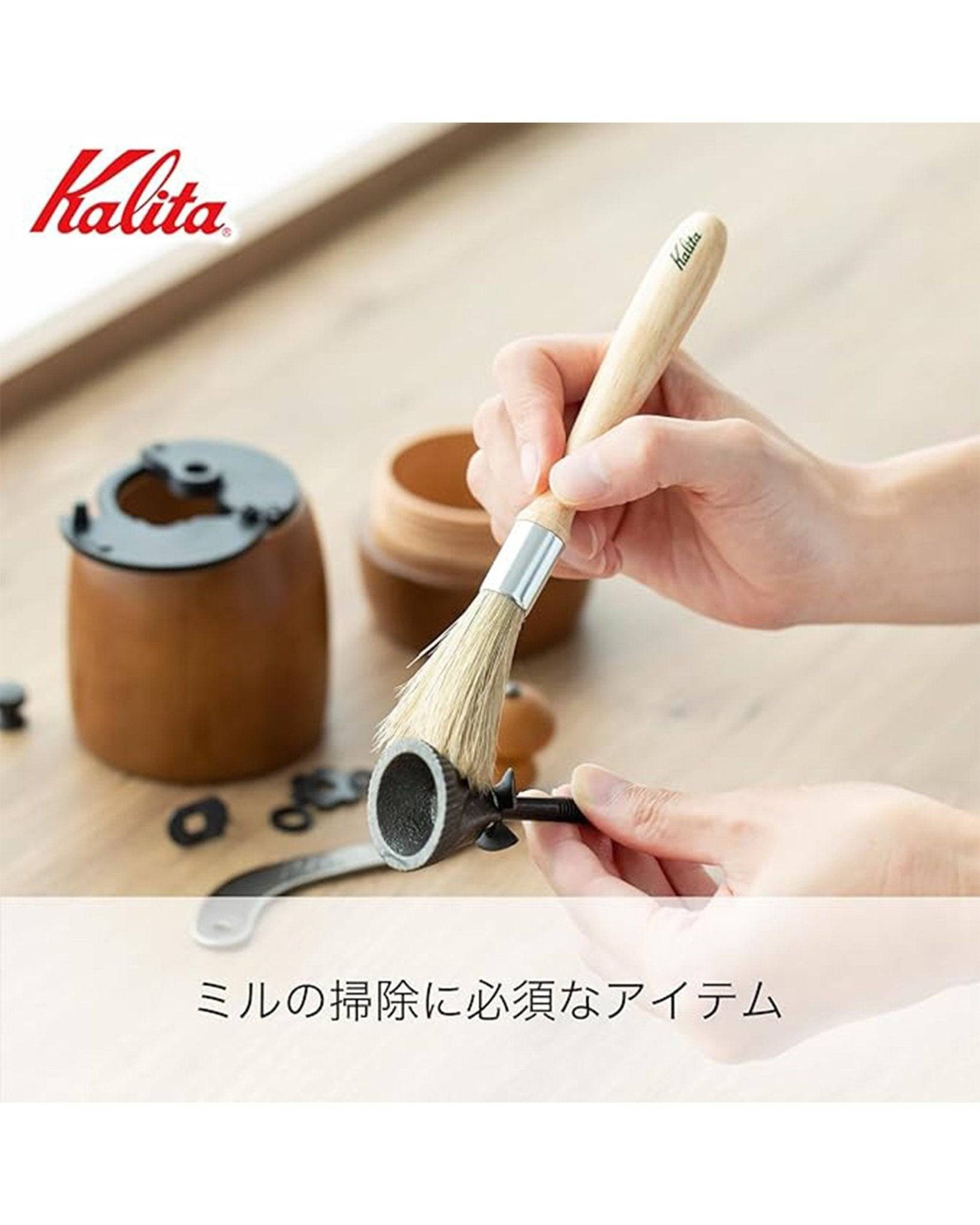 Kalita coffee cleaning brush with wooden handle being used to clean coffee grinder parts, showcasing its effectiveness in removing coffee residue from equipment