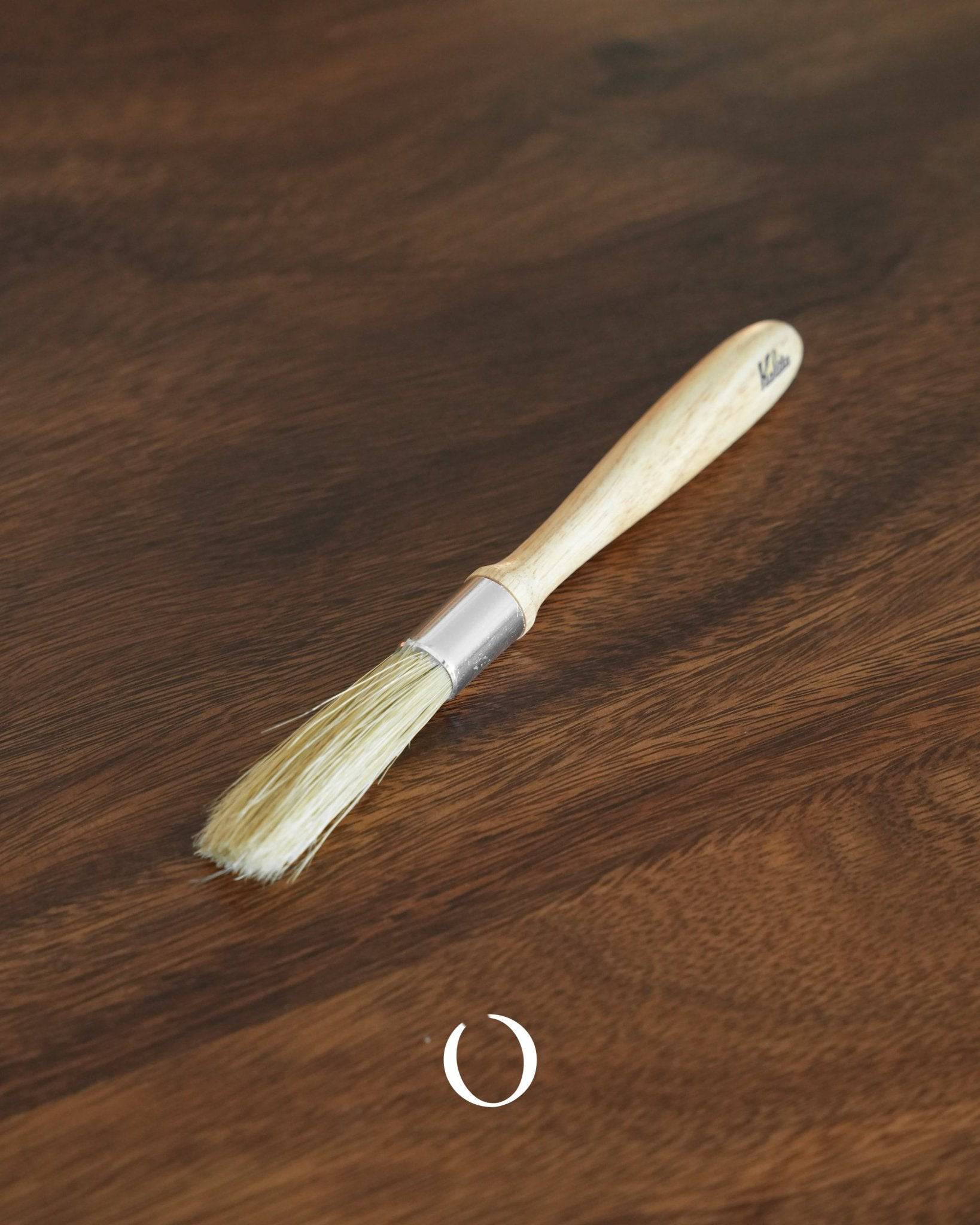 Kalita coffee cleaning brush with wooden handle and bristles, lying on a dark wooden surface, showcasing its compact design for efficient grinder maintenance