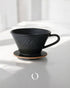 Kalita MI185 ceramic pour-over coffee dripper in matte black, featuring a wide base and Kalita branding, placed on a wooden coaster against a white background with soft shadows