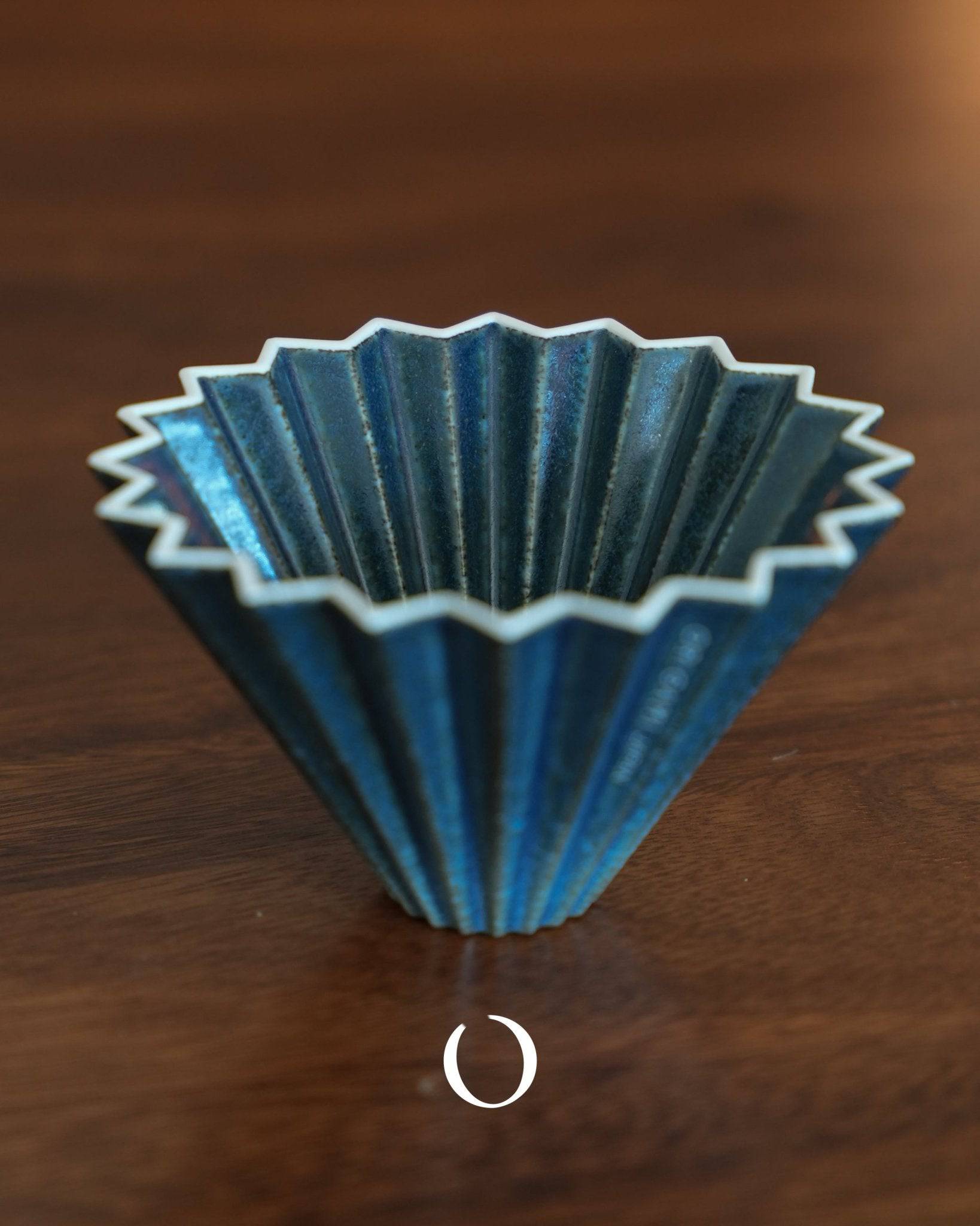 Limited edition ORIGAMI Dripper S in sukumo blue, featuring a unique indigo-dyed ceramic design with 20 ribbed folds for optimal coffee extraction, placed on a wooden surface.