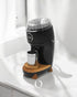 Niche Duo coffee grinder with sleek black design, transparent lid, wooden base, and metal cup positioned on white countertop, showcasing professional-grade home grinding experience