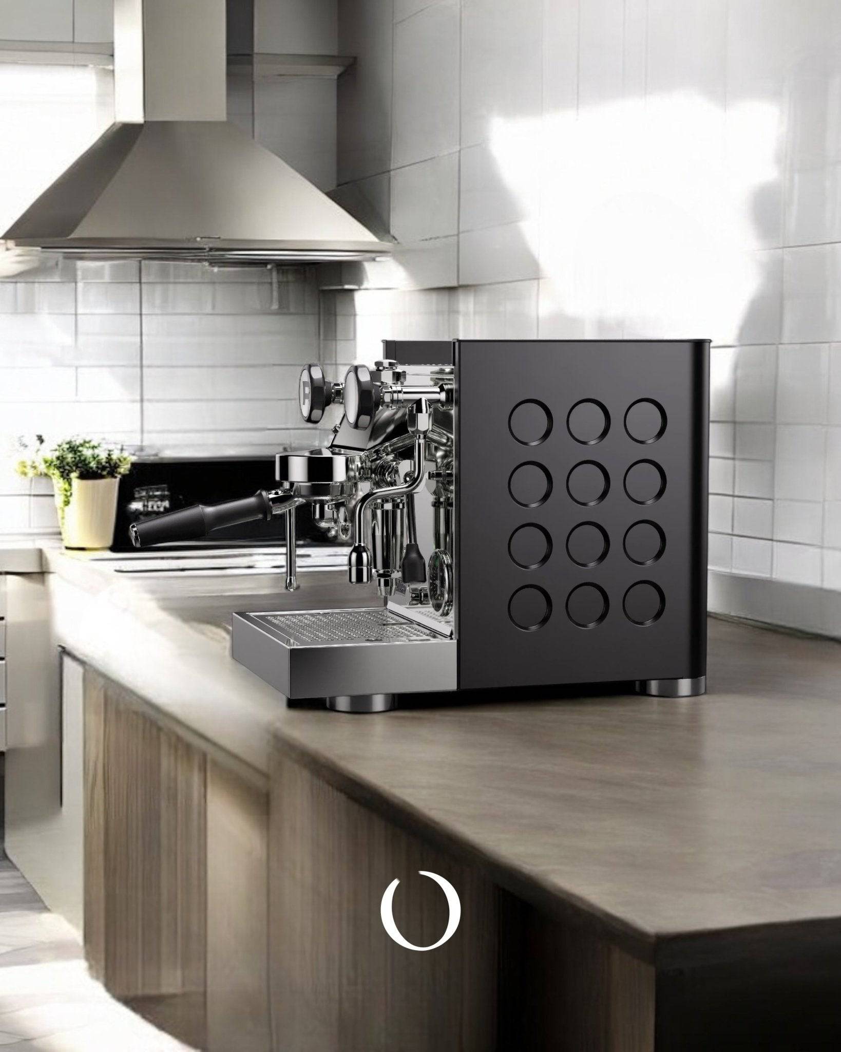 Sleek black Rocket Appartamento TCA espresso machine on modern kitchen counter, featuring circular design elements and professional-grade brewing components. Stainless steel range hood visible in background.
