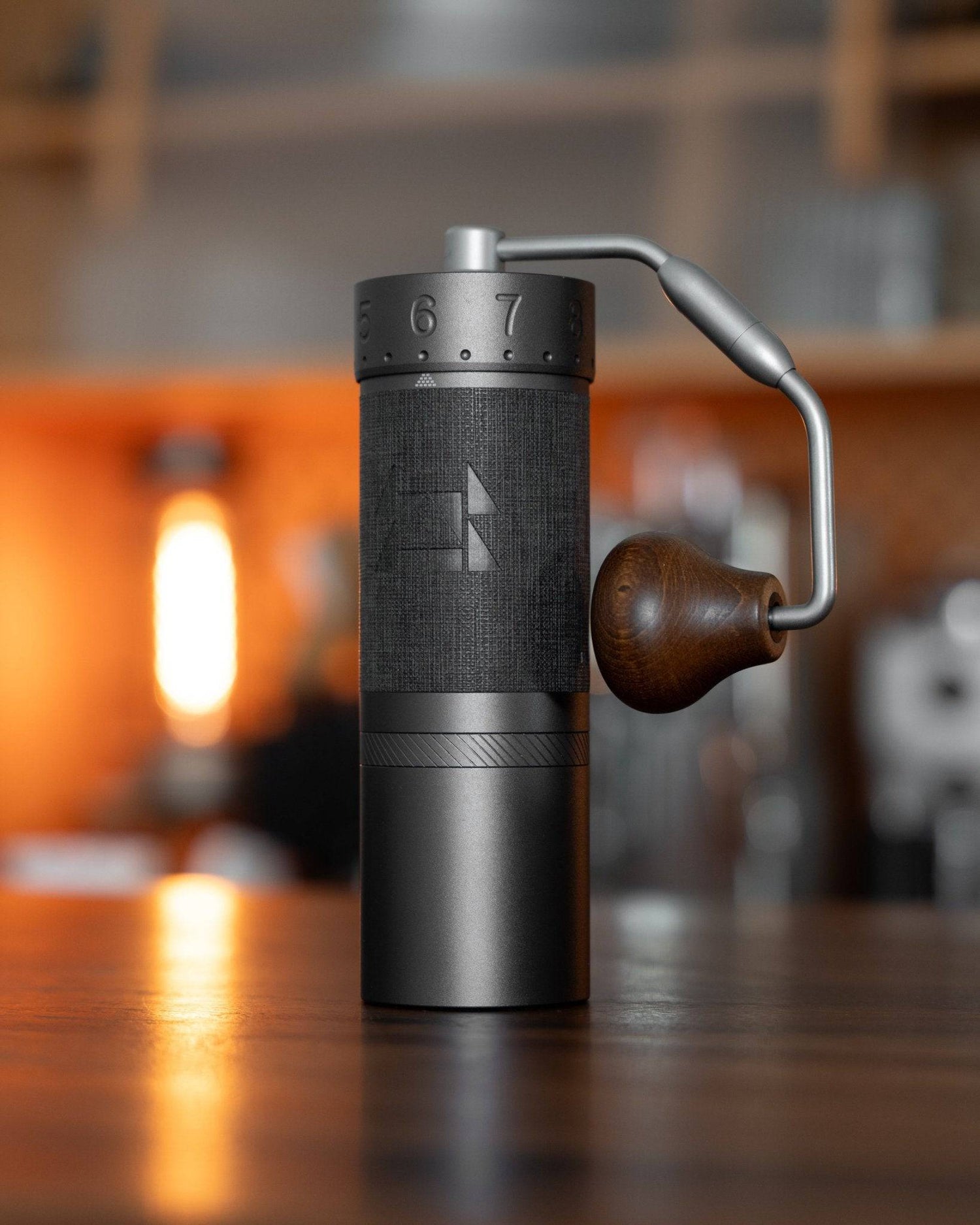 1zpresso J MAXS manual coffee grinder with sleek black design, wooden handle, and precise adjustment ring, displayed on a warm-toned countertop in a cozy kitchen setting