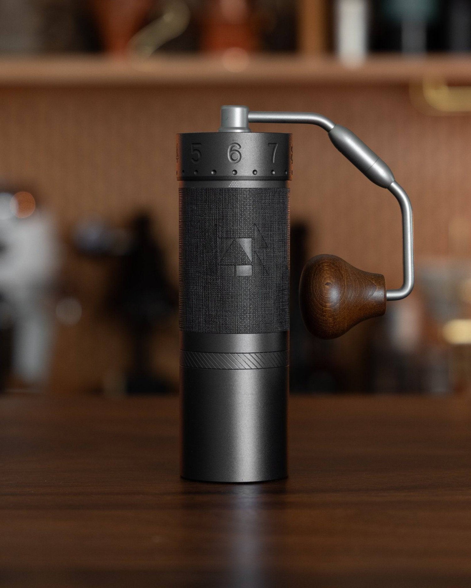 1zpresso J MAXS manual coffee grinder with sleek black design, wooden handle, and adjustable grind settings, displayed on a wooden countertop in a kitchen setting