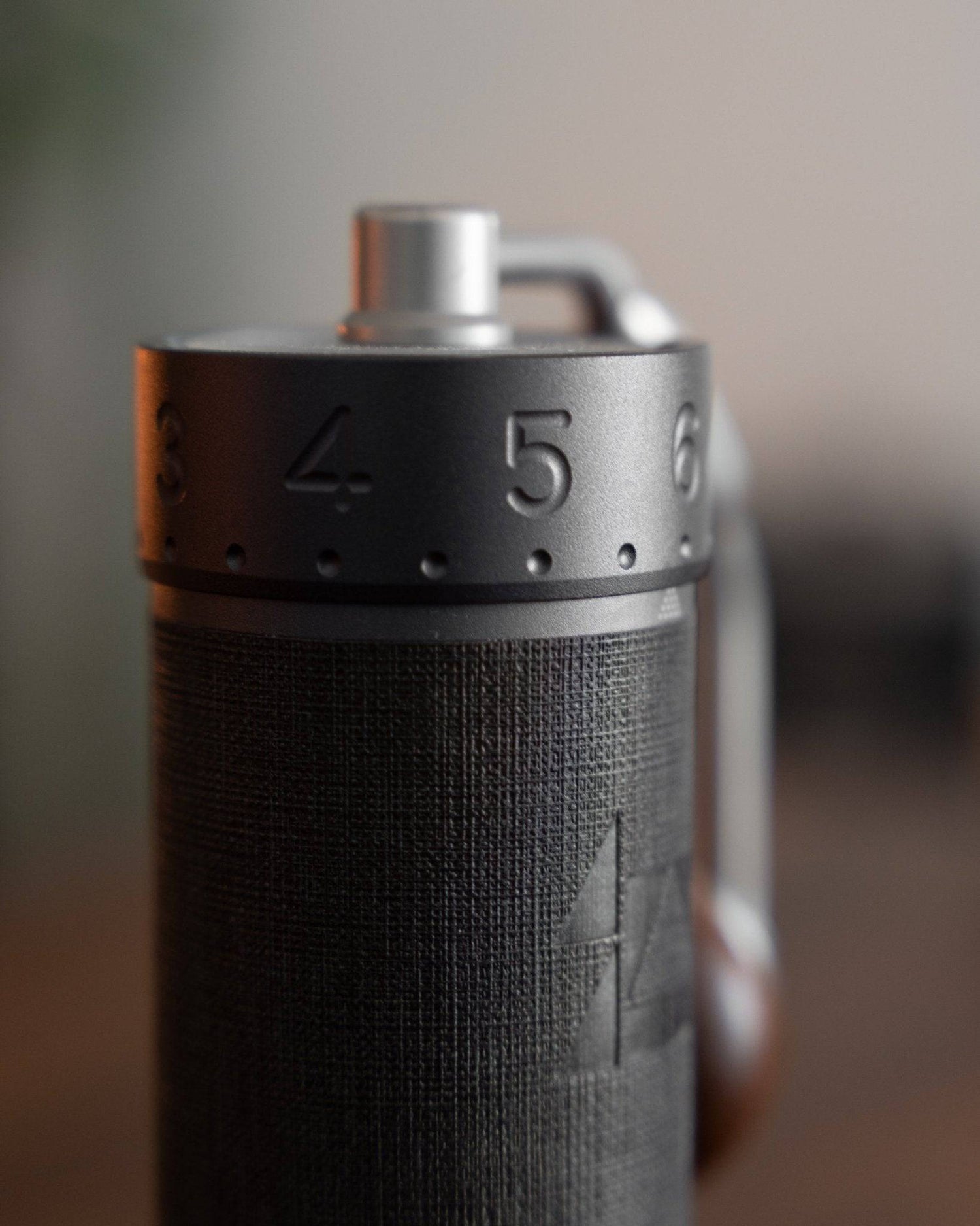 Close-up view of 1zpresso J MAXS manual coffee grinder, showing textured black body with silver adjustment ring and handle, highlighting precision grind settings and ergonomic design for espresso brewing