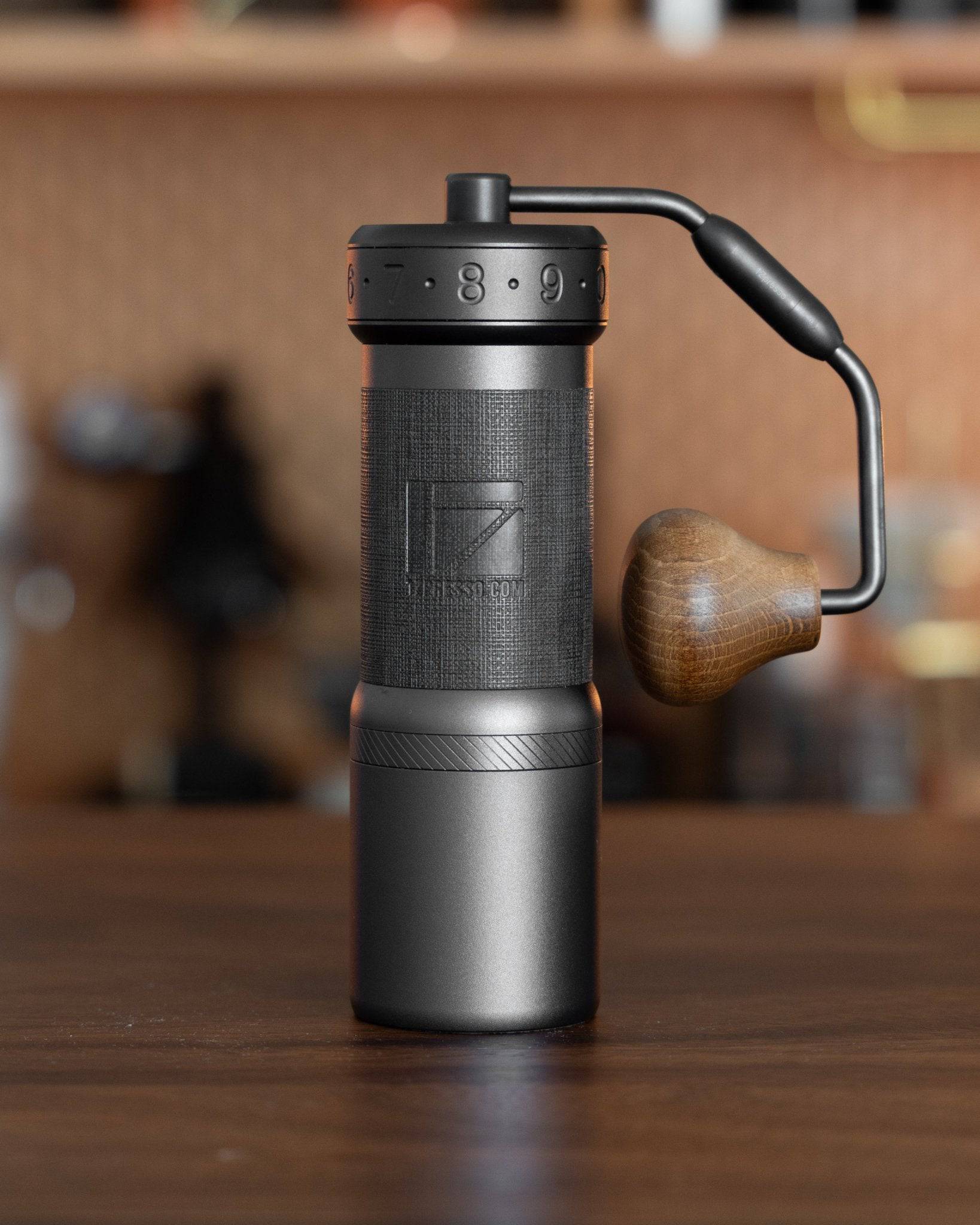 1Zpresso K-Ultra manual coffee grinder with foldable handle, sleek black design, adjustable grind settings, and wooden knob, displayed on wooden surface with blurred background