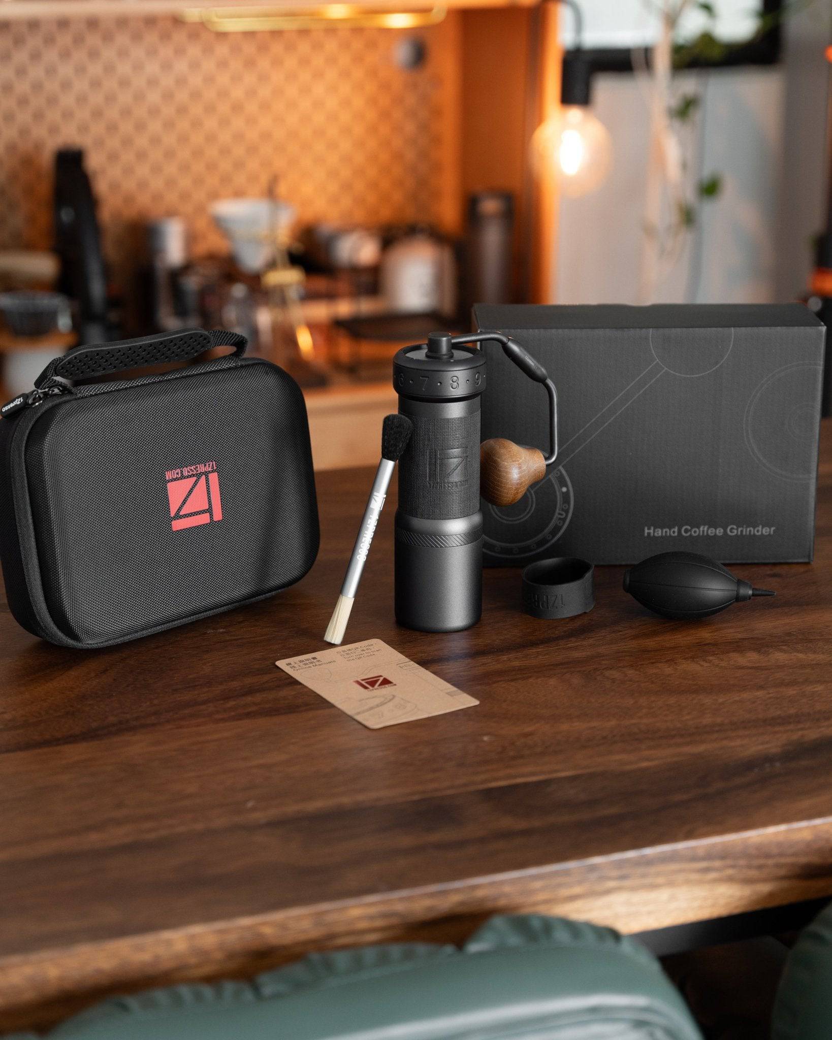 1Zpresso K-Ultra hand coffee grinder set on wooden table, including grinder, carrying case, box, and accessories, with blurred kitchen background
