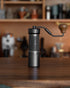 1Zpresso K-Ultra manual coffee grinder with foldable handle on wooden surface, showcasing sleek black design and compact size, perfect for precision grinding at home or while traveling