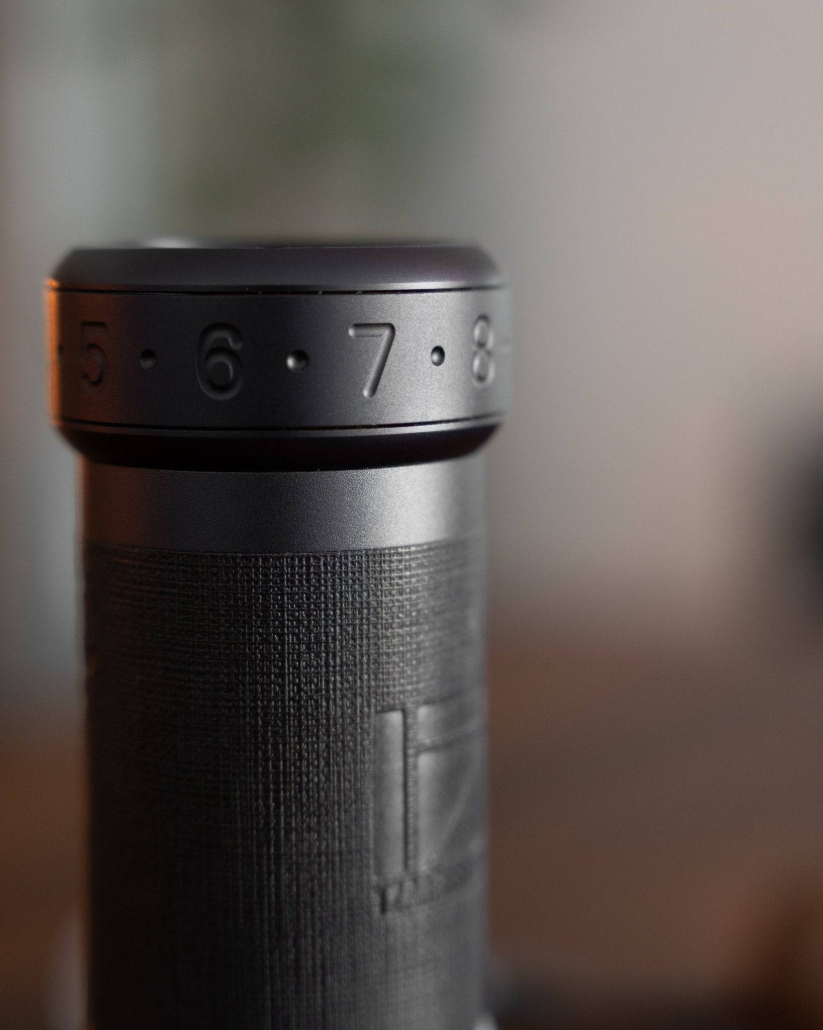 Close-up of 1Zpresso K-Ultra manual coffee grinder, showing precise adjustment ring with numbers 5-6-7-8 and textured black aluminum body with brand logo embossed.