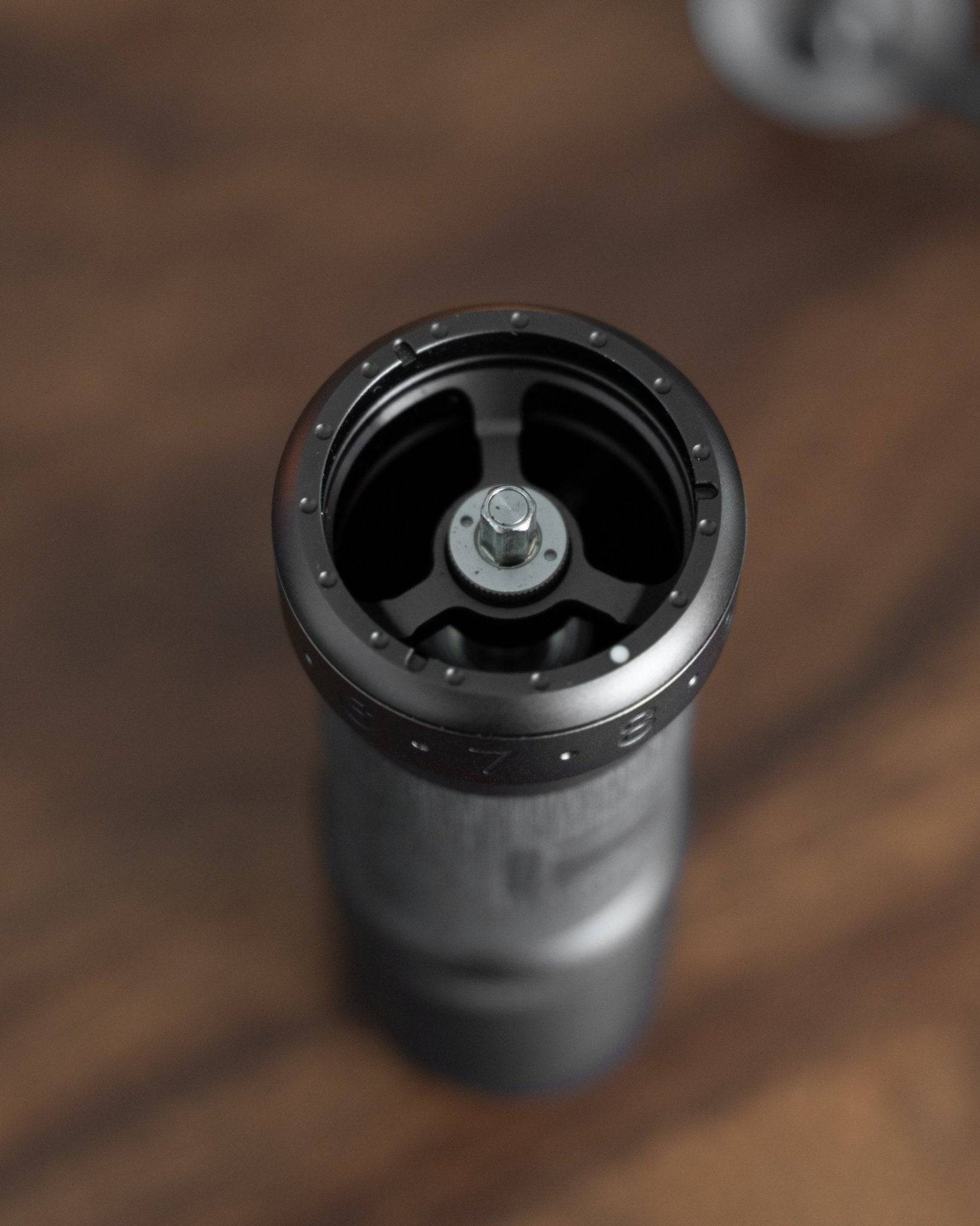 Top view of 1Zpresso K-Ultra manual coffee grinder, showing black cylindrical body and internal burr mechanism on wooden surface