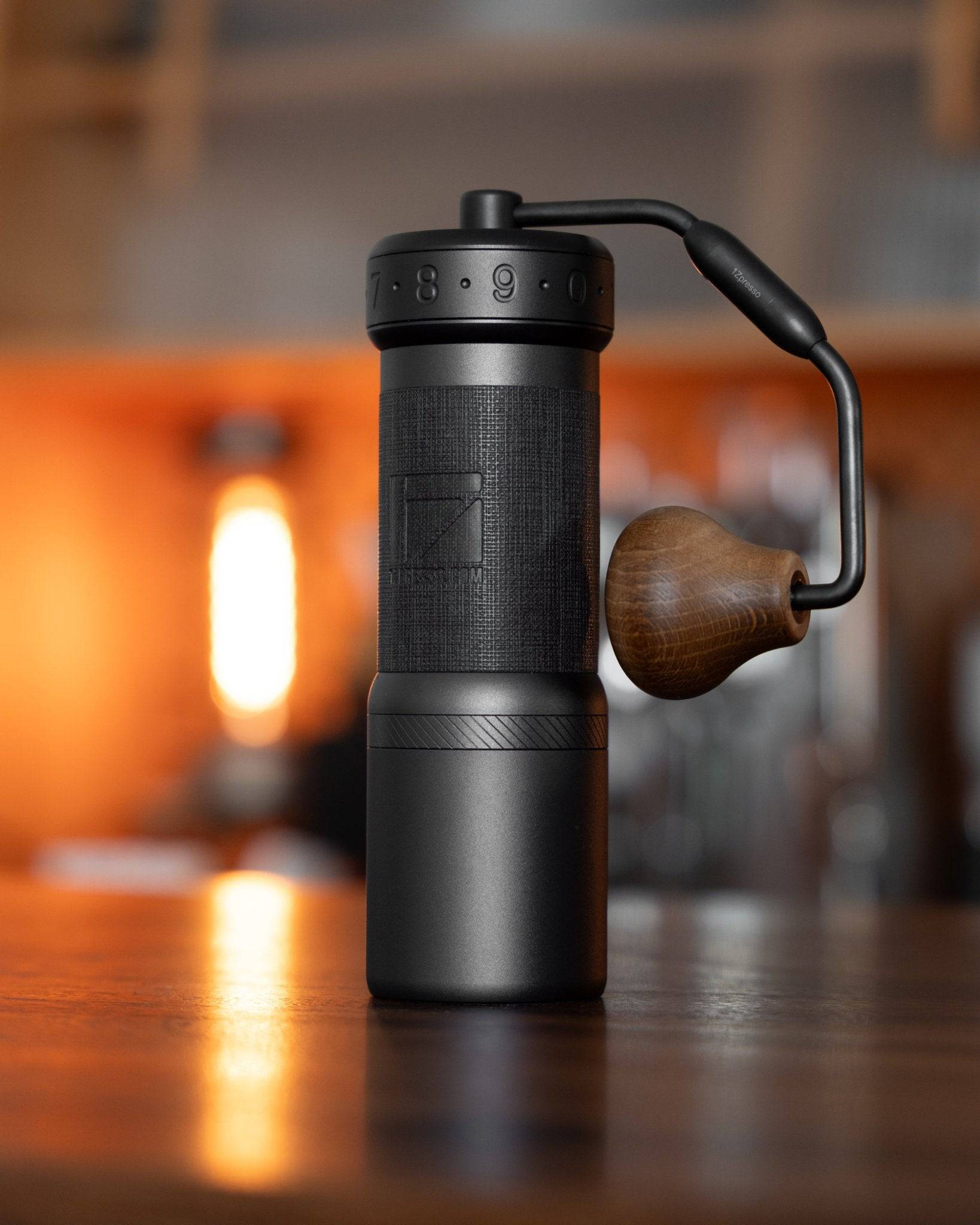 1Zpresso K-Ultra manual coffee grinder with foldable handle, sleek black design, wooden knob, on wooden table with warm lighting in background