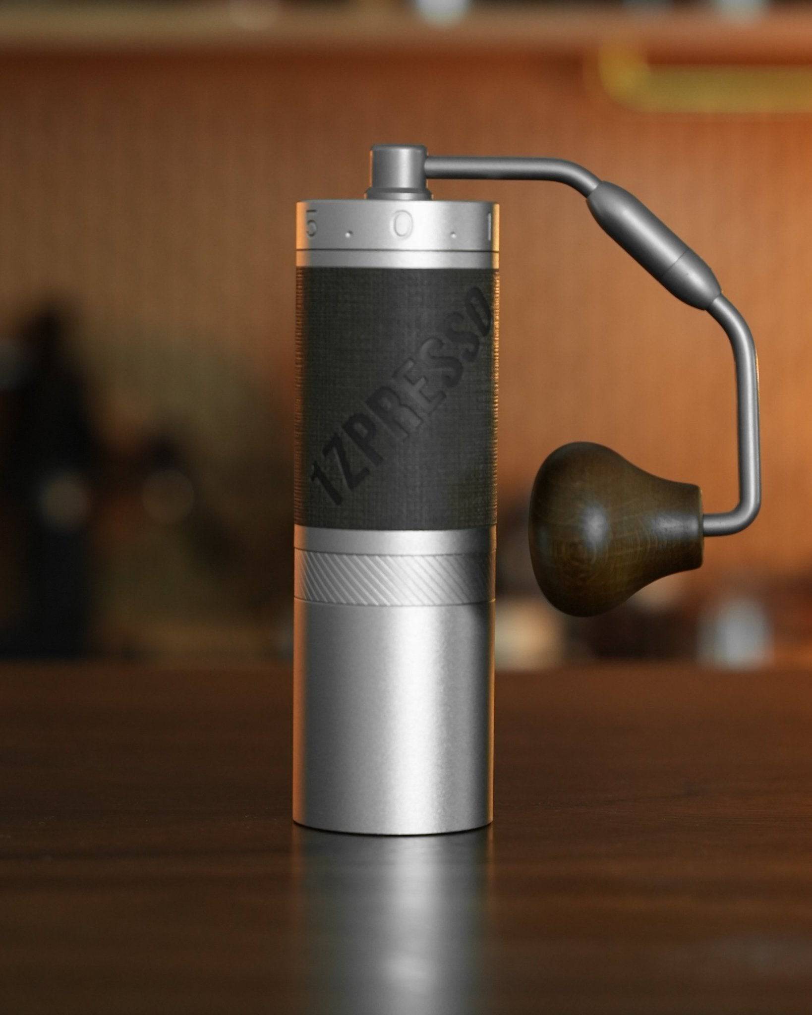 1Zpresso X-Pro-S manual coffee grinder with sleek aluminum body, black textured grip, and ergonomic wooden handle on wooden surface, showcasing its portable and professional design for coffee enthusiasts