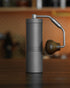 1Zpresso X-Ultra manual coffee grinder with sleek metal body, adjustable grind settings, and ergonomic wooden handle, positioned on wooden surface in kitchen setting