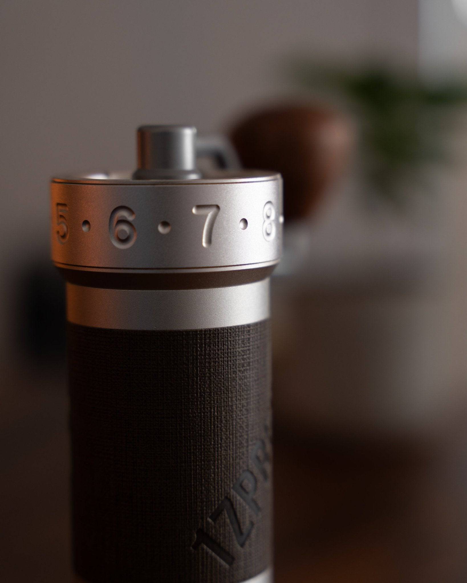 Close-up of 1zpresso ZP6 manual coffee grinder, showing silver adjustment ring with numbers, textured black body, and precise design for optimal coffee grinding experience.