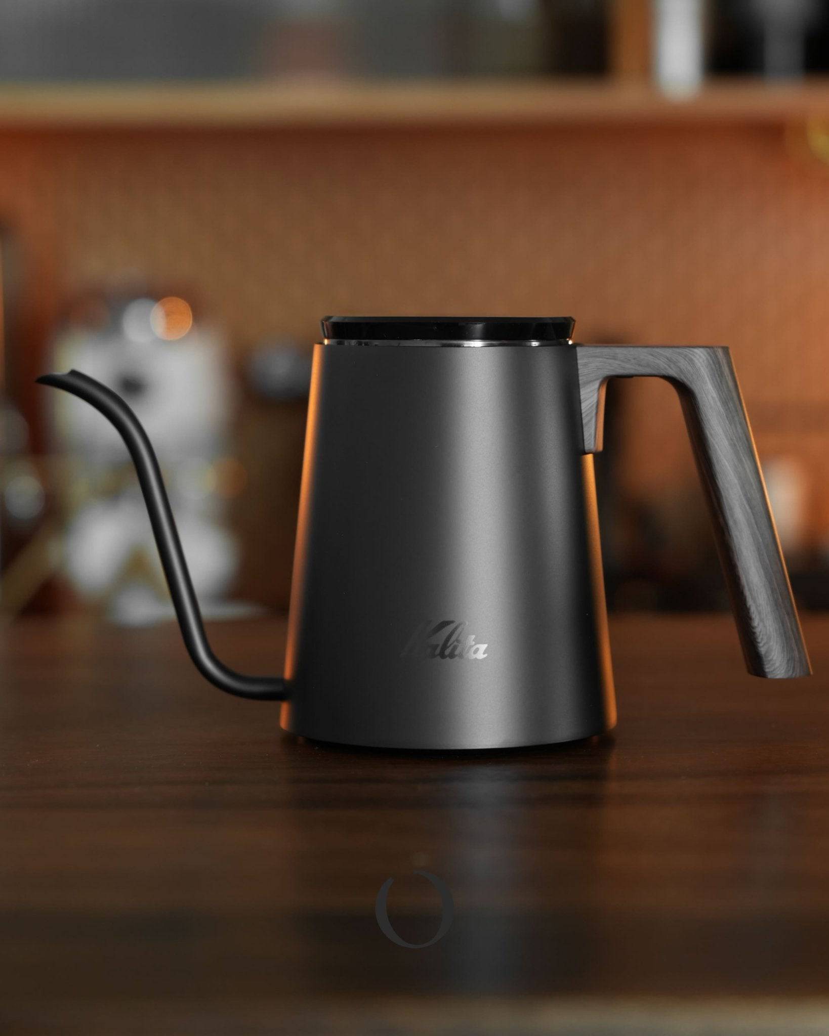 Kalita KDP-800 pour-over kettle in sleek black, featuring a gooseneck spout and ergonomic handle, displayed on wooden surface in a cozy kitchen setting, perfect for precision coffee brewing