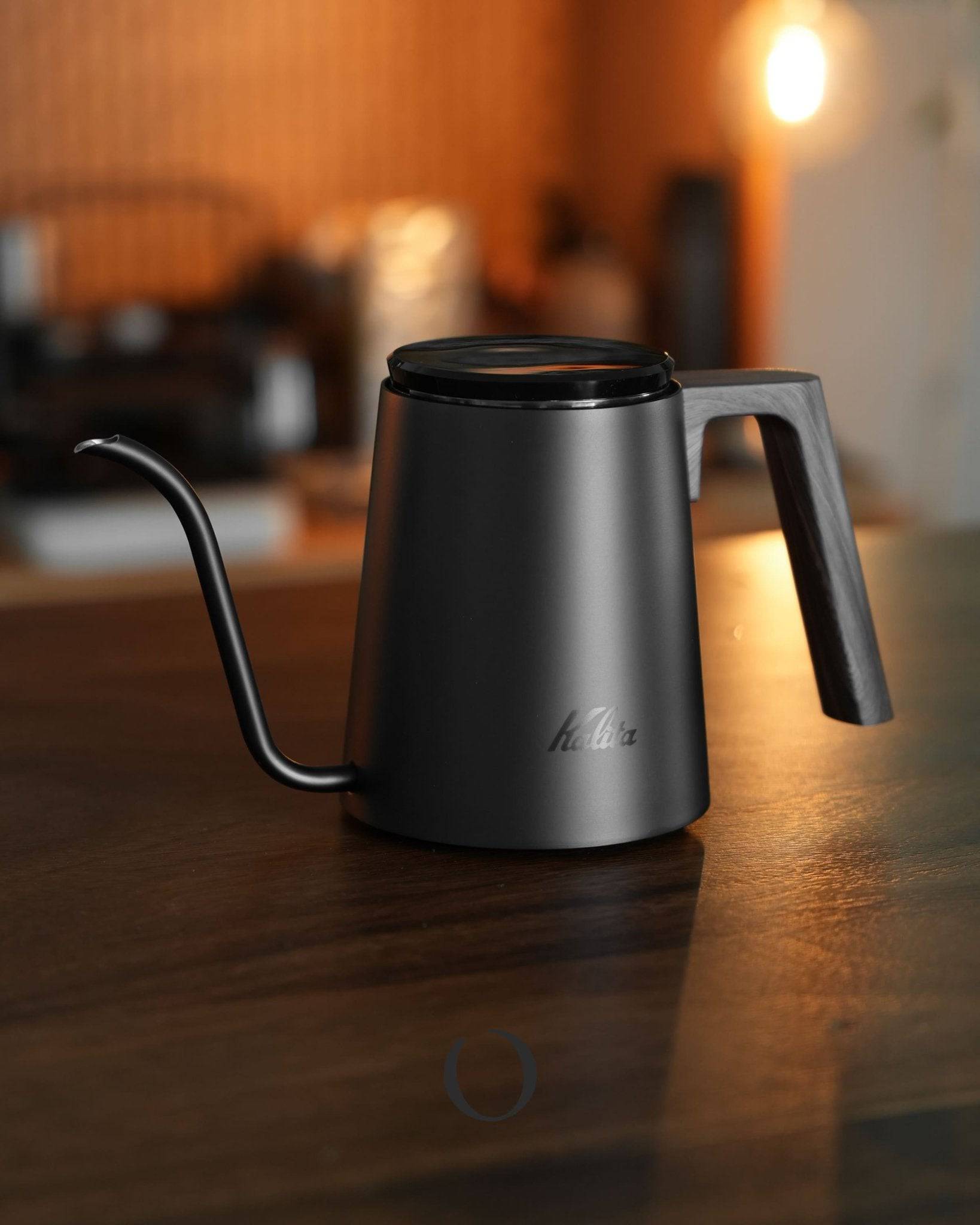 Kalita KDP-800 black walnut wood grain coffee pour-over kettle, 800ml capacity, sleek design with gooseneck spout, sitting on wooden table in warm-lit kitchen setting