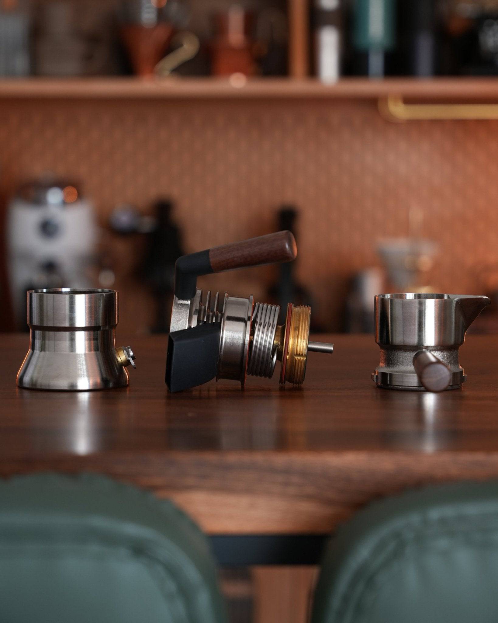 Disassembled components of 9Barista espresso maker on wooden countertop, showcasing stainless steel parts and wooden handle against copper-toned backsplash in kitchen setting