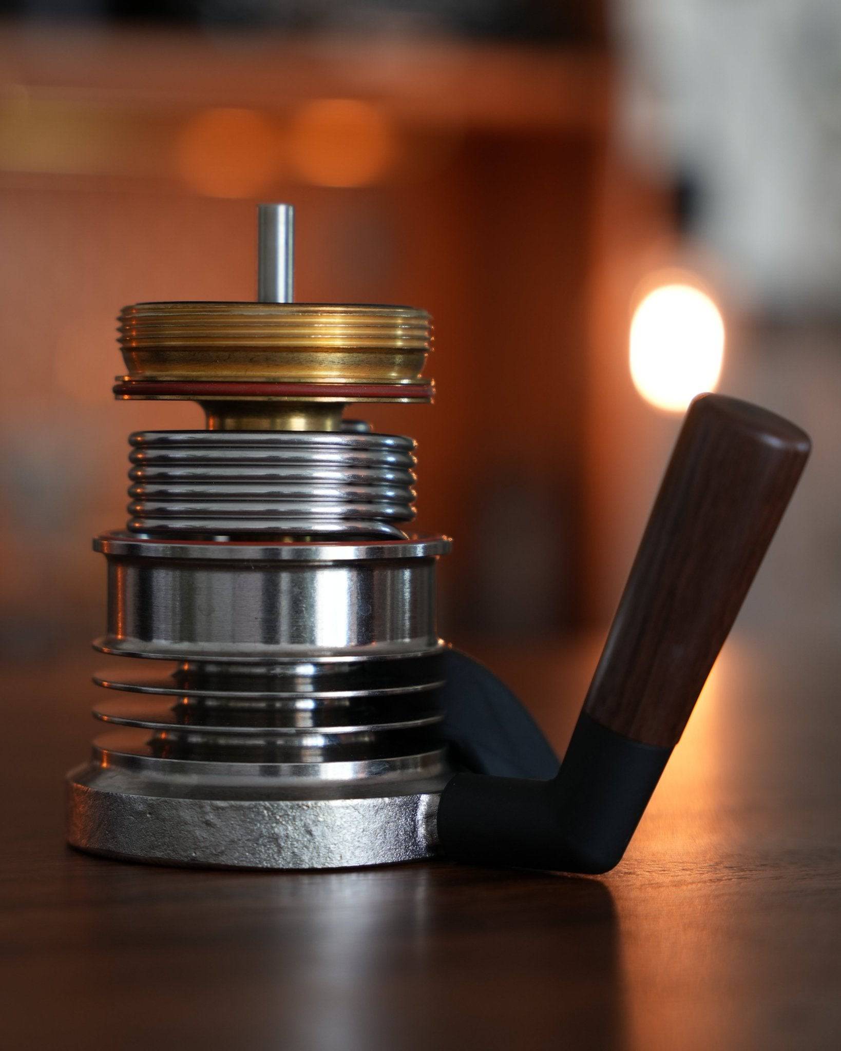 Disassembled 9Barista espresso machine components, showing stainless steel and brass parts with a wooden handle, illuminated by warm background lighting