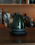 Brewista Artisan temperature-controlled kettle with gooseneck spout on wooden countertop, featuring sleek dark green design and digital base for precise brewing