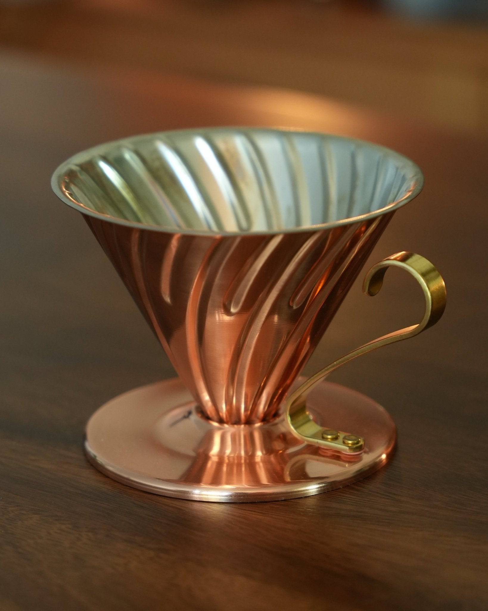 HARIO V60 02 copper pour-over coffee dripper with conical shape, spiral ribs, and brass handle, showcasing Japanese craftsmanship and superior heat conductivity for optimal coffee extraction