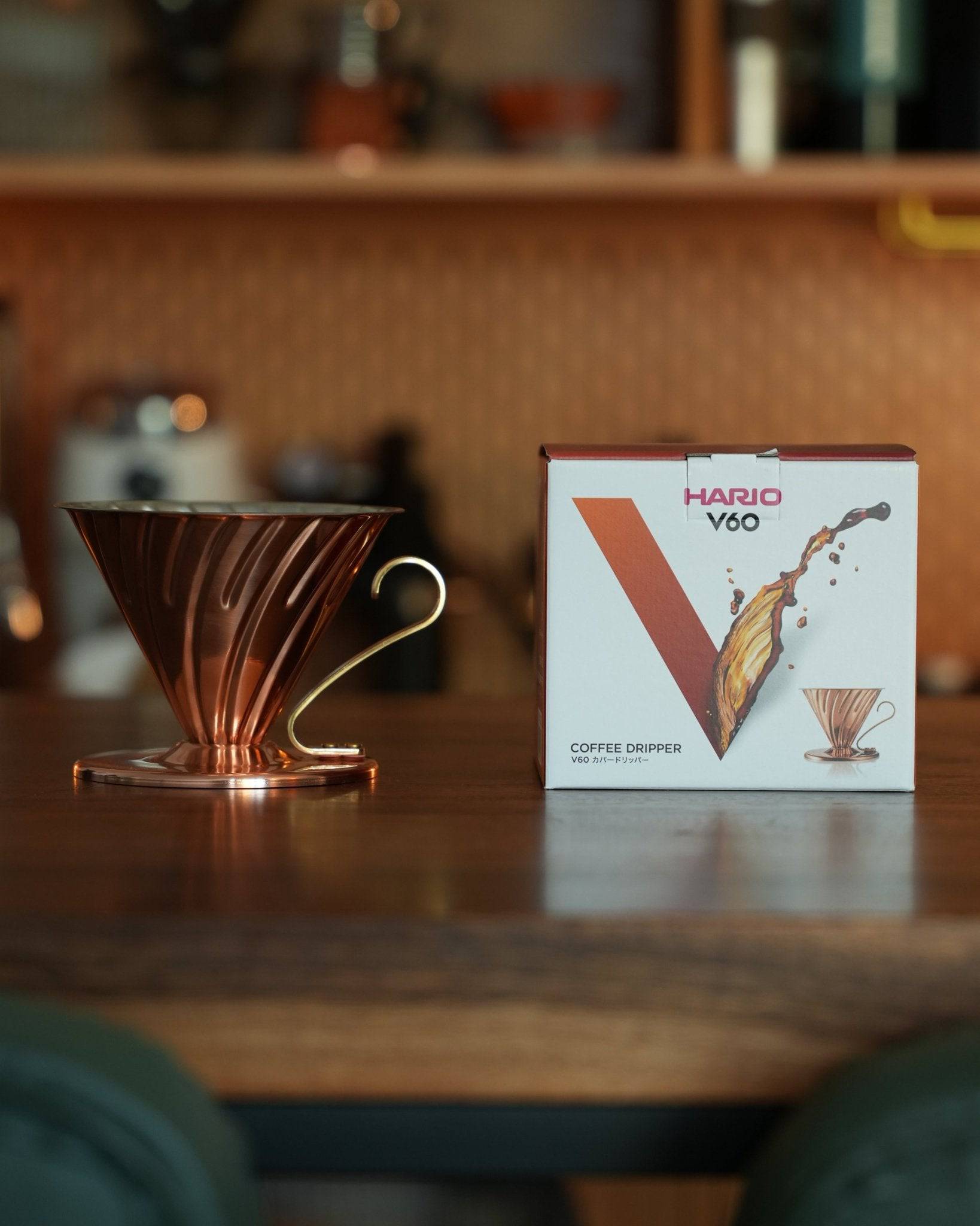 Copper HARIO V60 02 coffee dripper on wooden counter next to its product box, showcasing elegant design and premium quality for pour-over coffee brewing