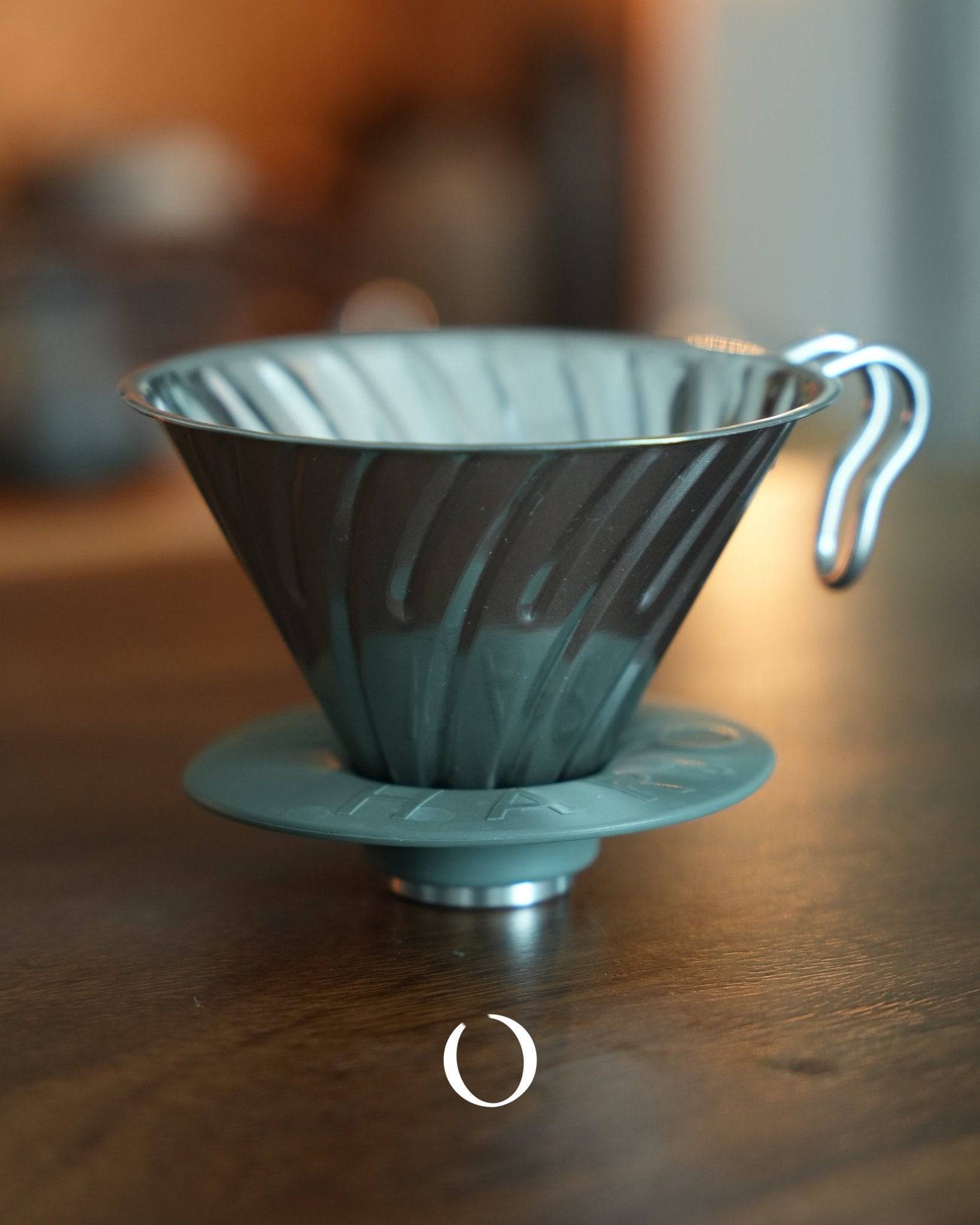 HARIO V60 stainless steel coffee dripper in silver, conical shape with spiral ribs, placed on wooden surface, showcasing its durable design for optimal coffee extraction