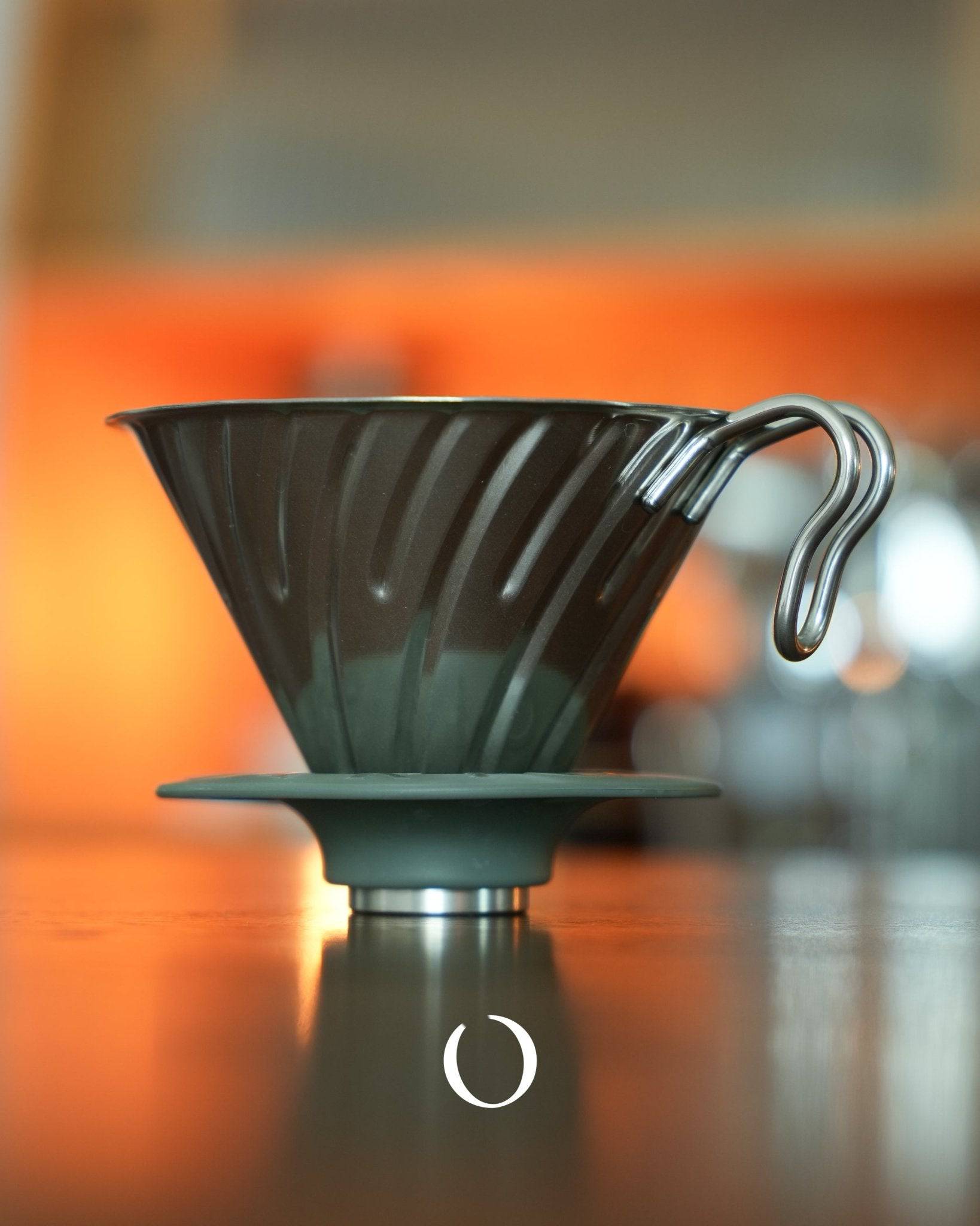 HARIO V60 02 stainless steel coffee dripper with conical design and spiral ribs, silver color, on orange background, showcasing its durable construction and efficient brewing capabilities for 1-4 cups of coffee.
